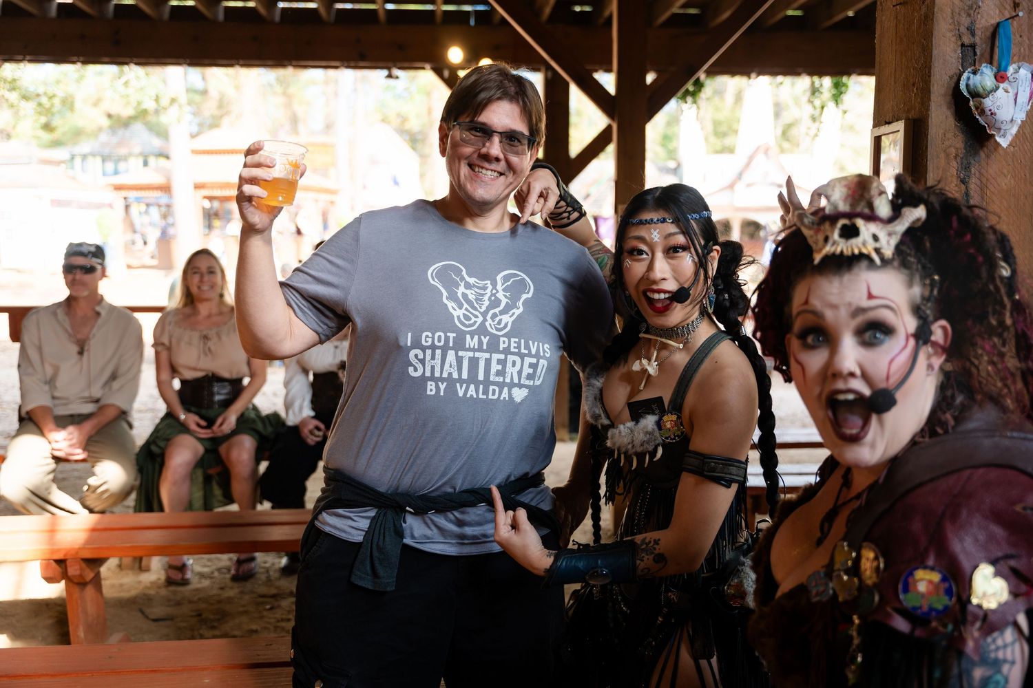 People gathered at a rustic outdoor bar enjoying drinks and socializing under a wooden shelter structure.