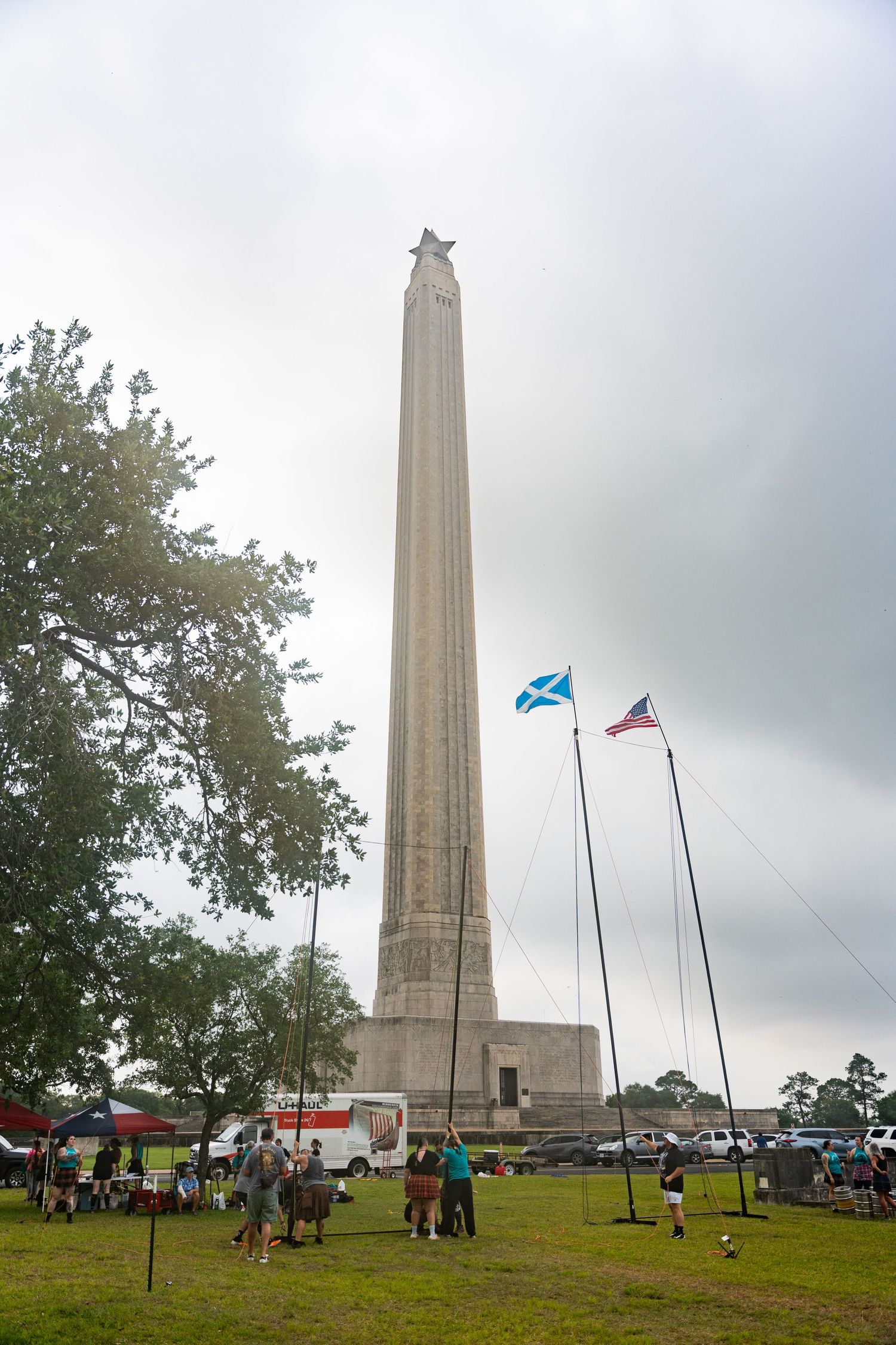 San Jacinto Monument obelisk with Scottish and American flags flying under cloudy skies at a Texas historical site.