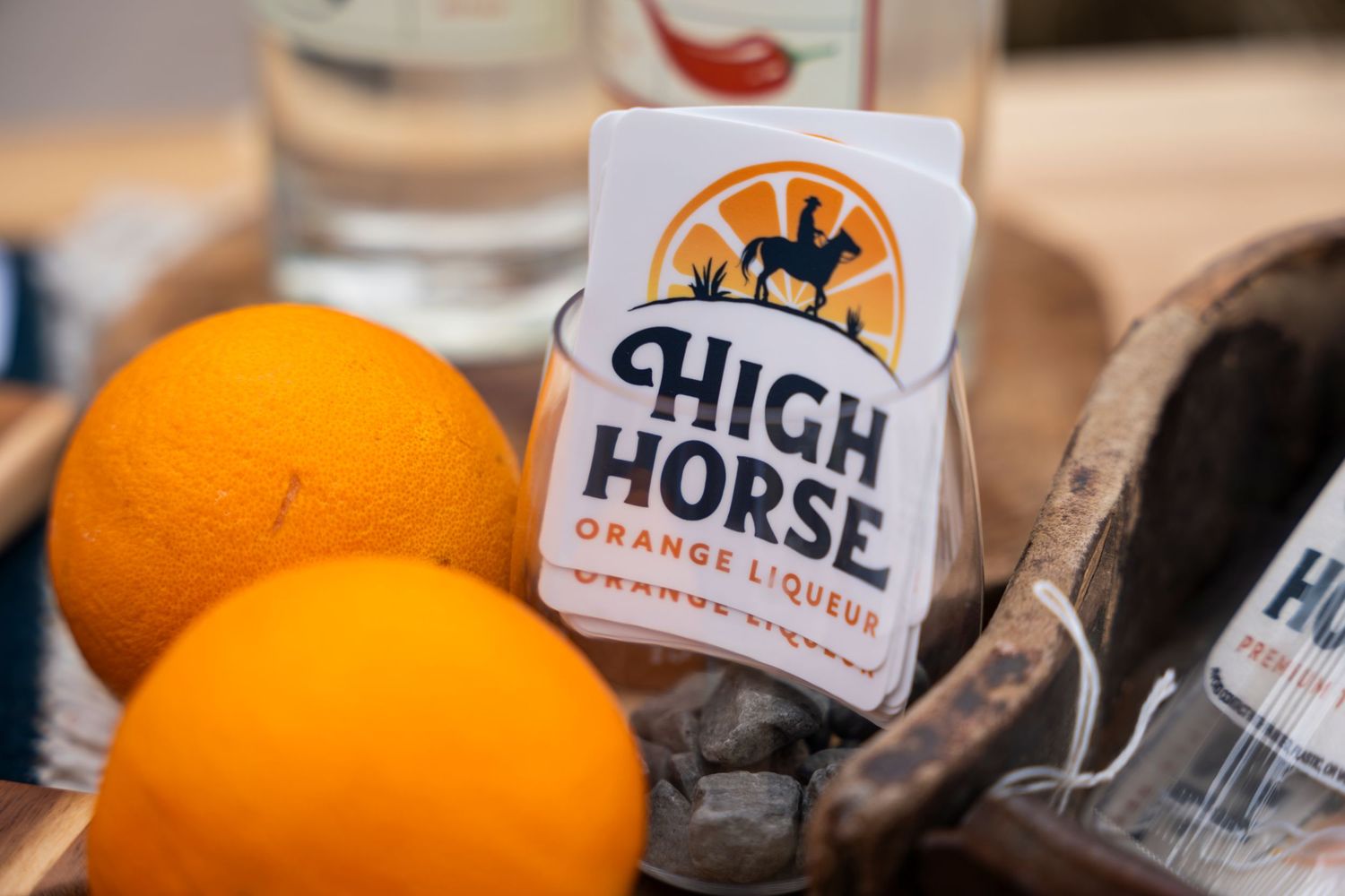 Orange juice and cocktail ingredients displayed on a wooden surface next to craft beverage bottles.