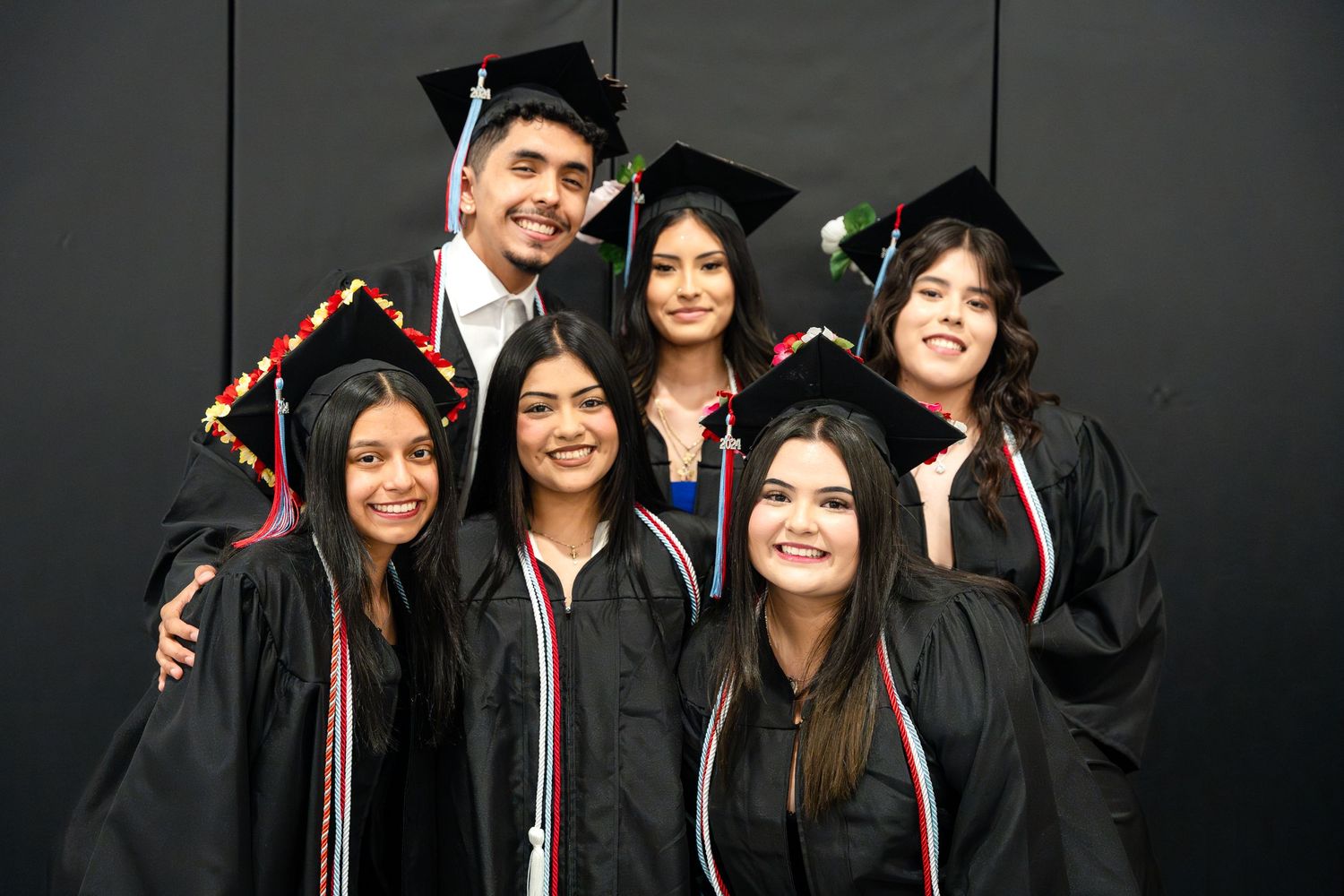 Group of graduates in black caps and gowns posing together for celebratory photo.