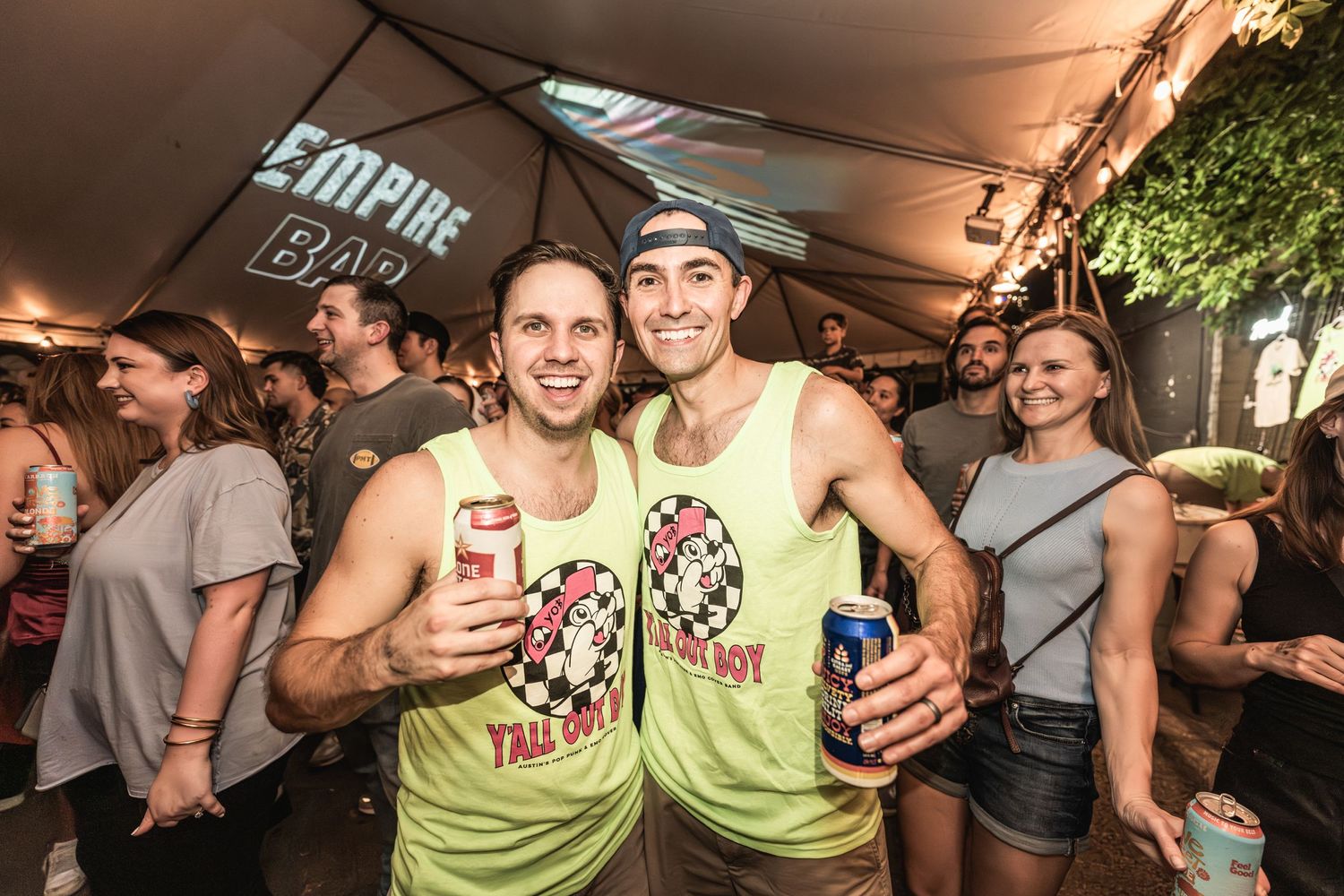 Festival-goers in matching tank tops enjoying outdoor summer party under tent lighting.