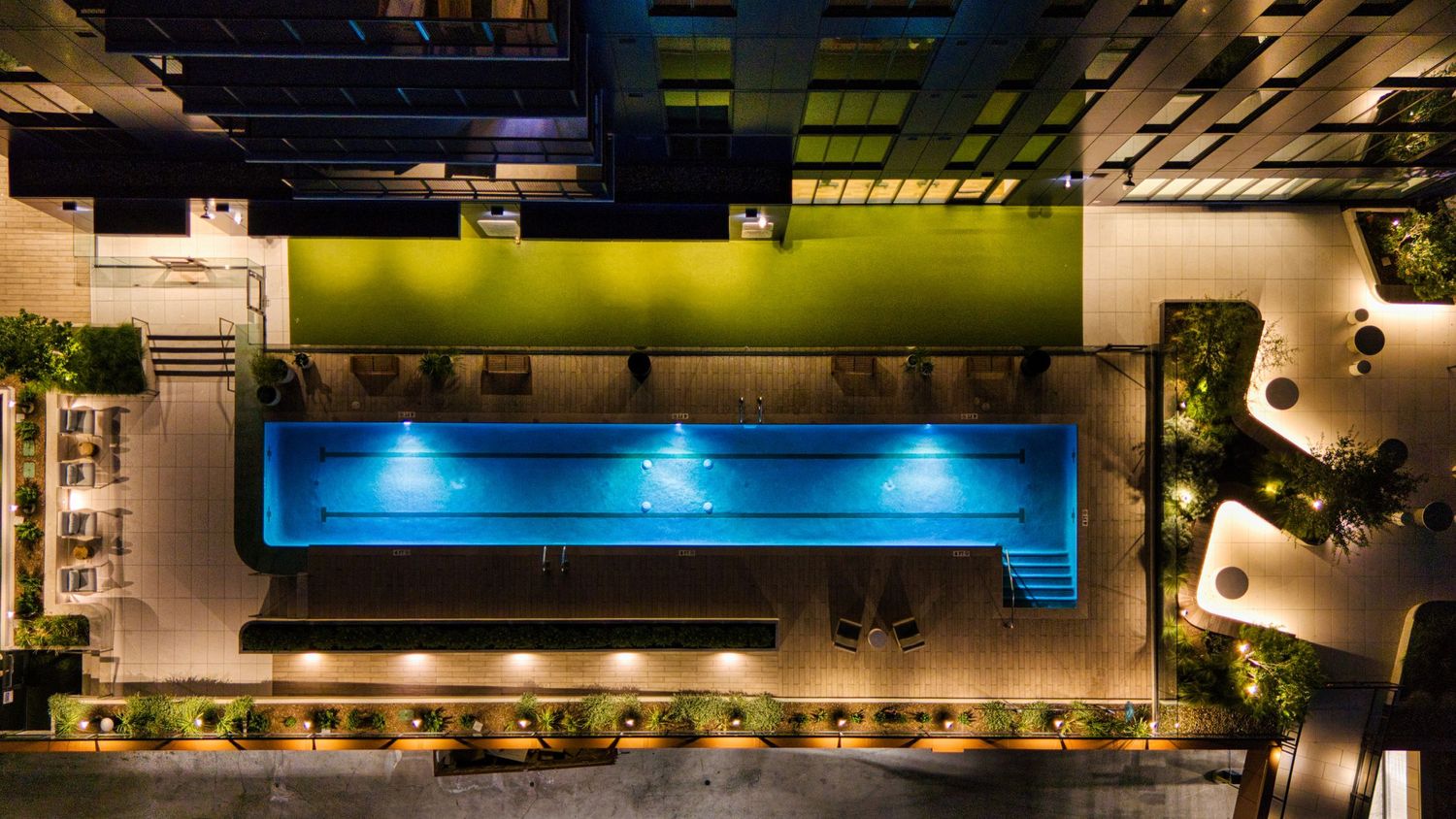 Overhead view of illuminated rooftop swimming pool with contemporary landscaping and seating areas.