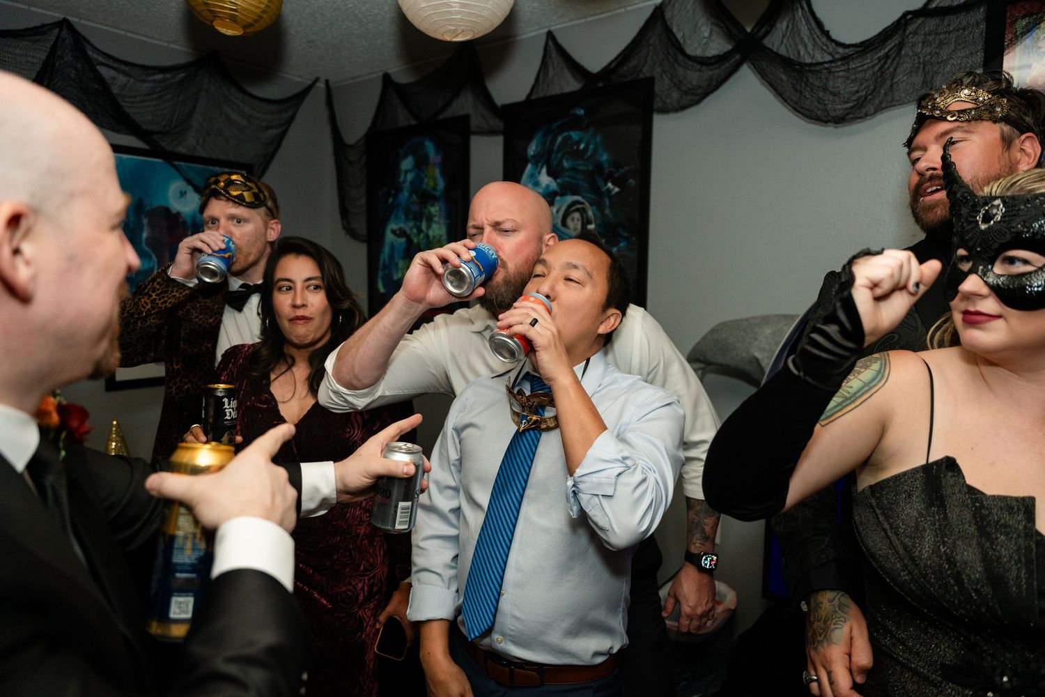 Party guests take shots and sip drinks at a lively indoor celebration with black decorations.