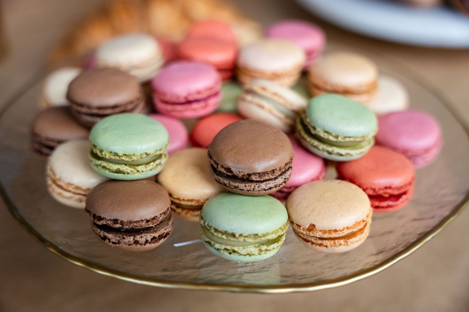 Colorful French macarons in pink, green, brown and beige arranged on a glass plate.