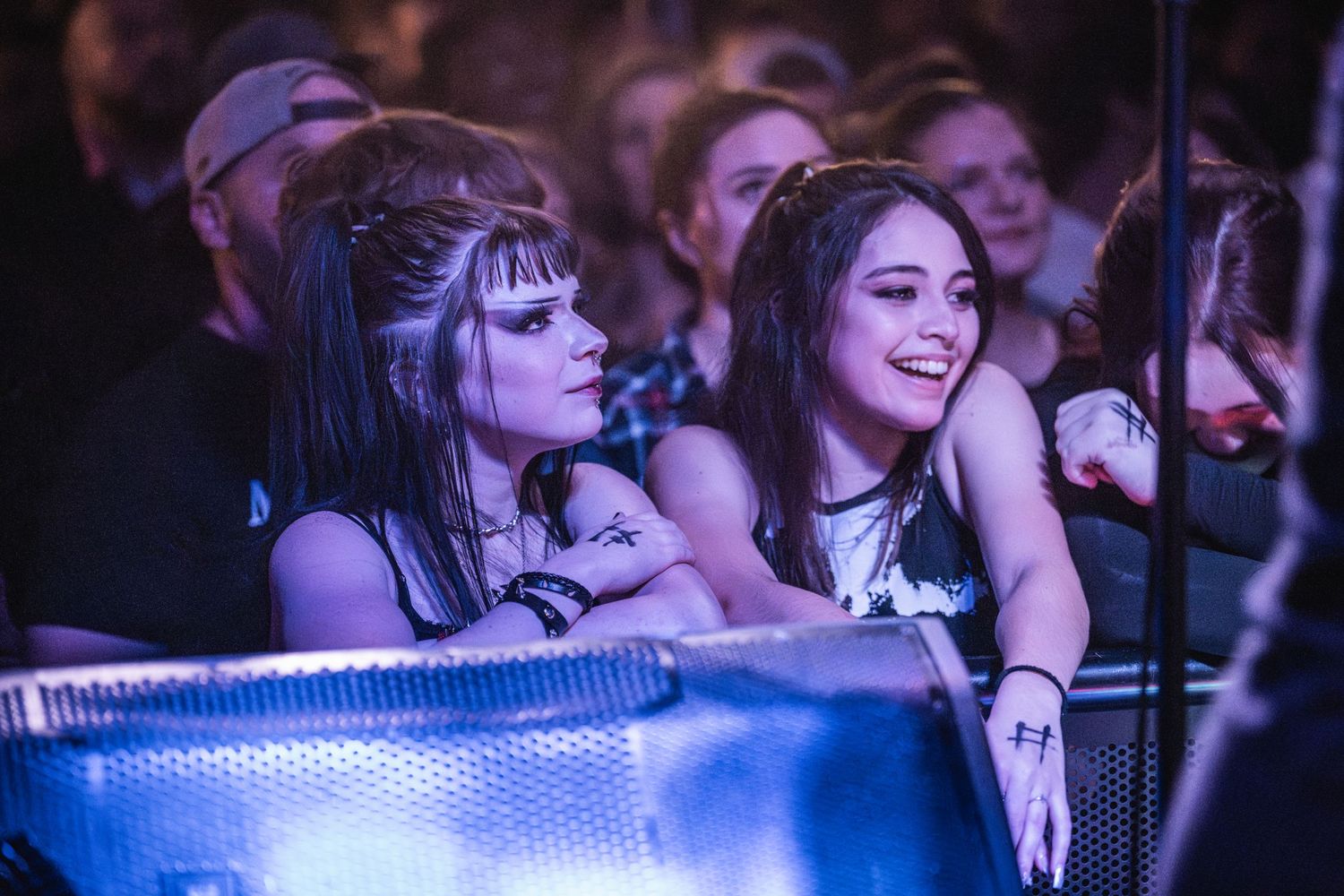 Concert attendees lean on barrier near stage while enjoying live music performance.