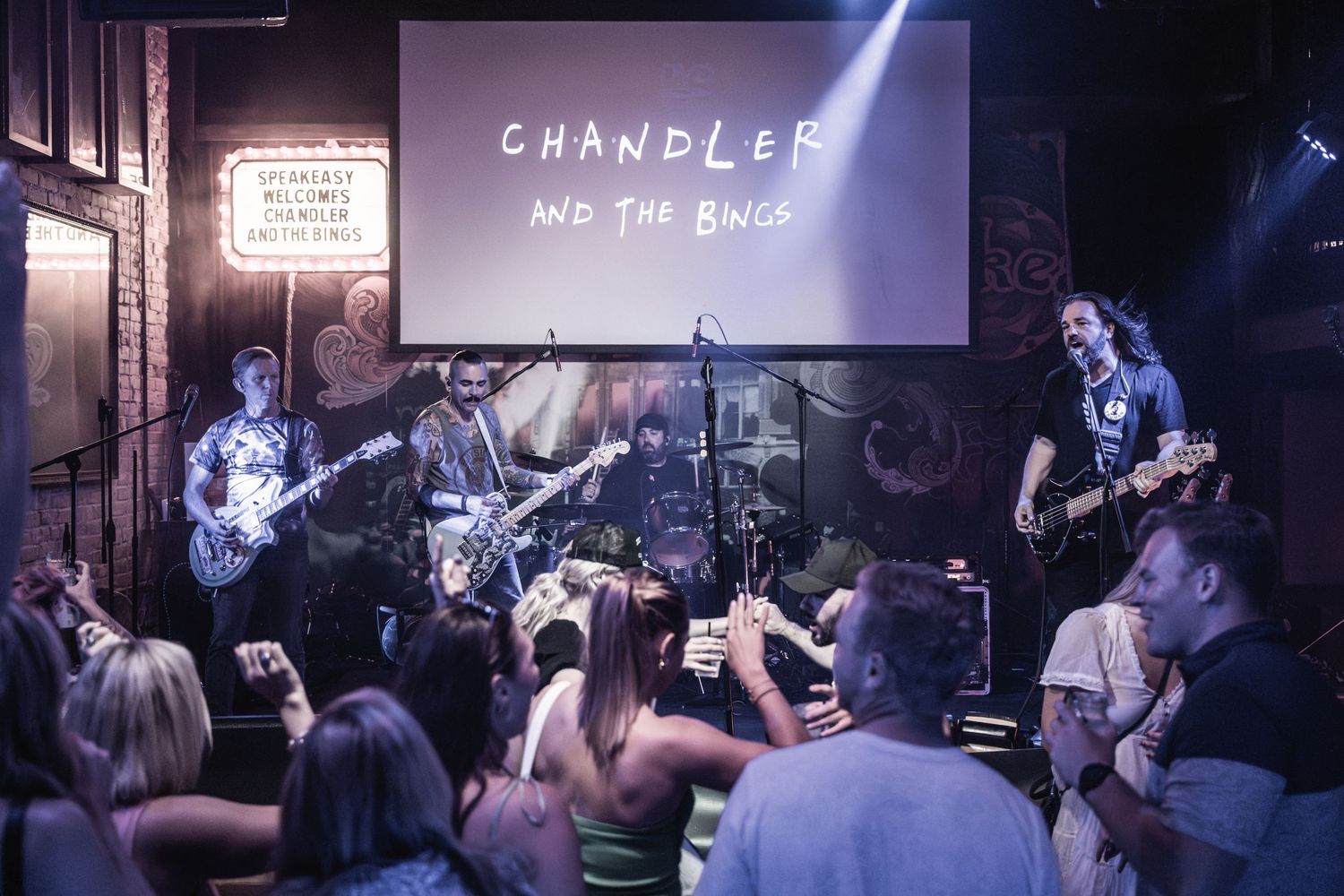 Band performs under 'Chandler' projection screen while audience members capture photos on phones.