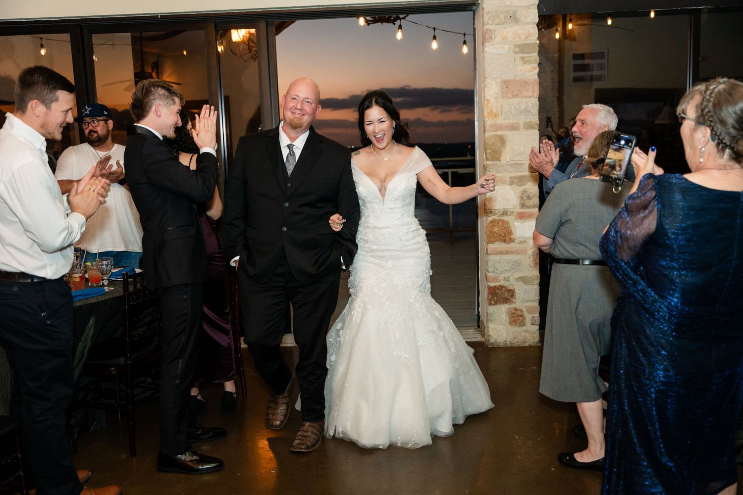 Wedding couple making grand entrance at reception while guests applaud.