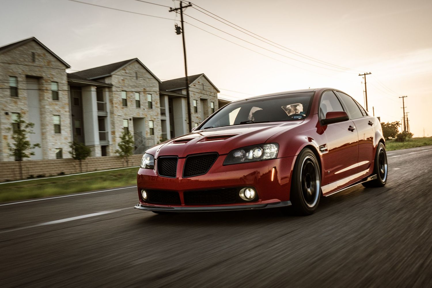 Lowered red Pontiac G8 with custom wheels photographed in motion near apartments.