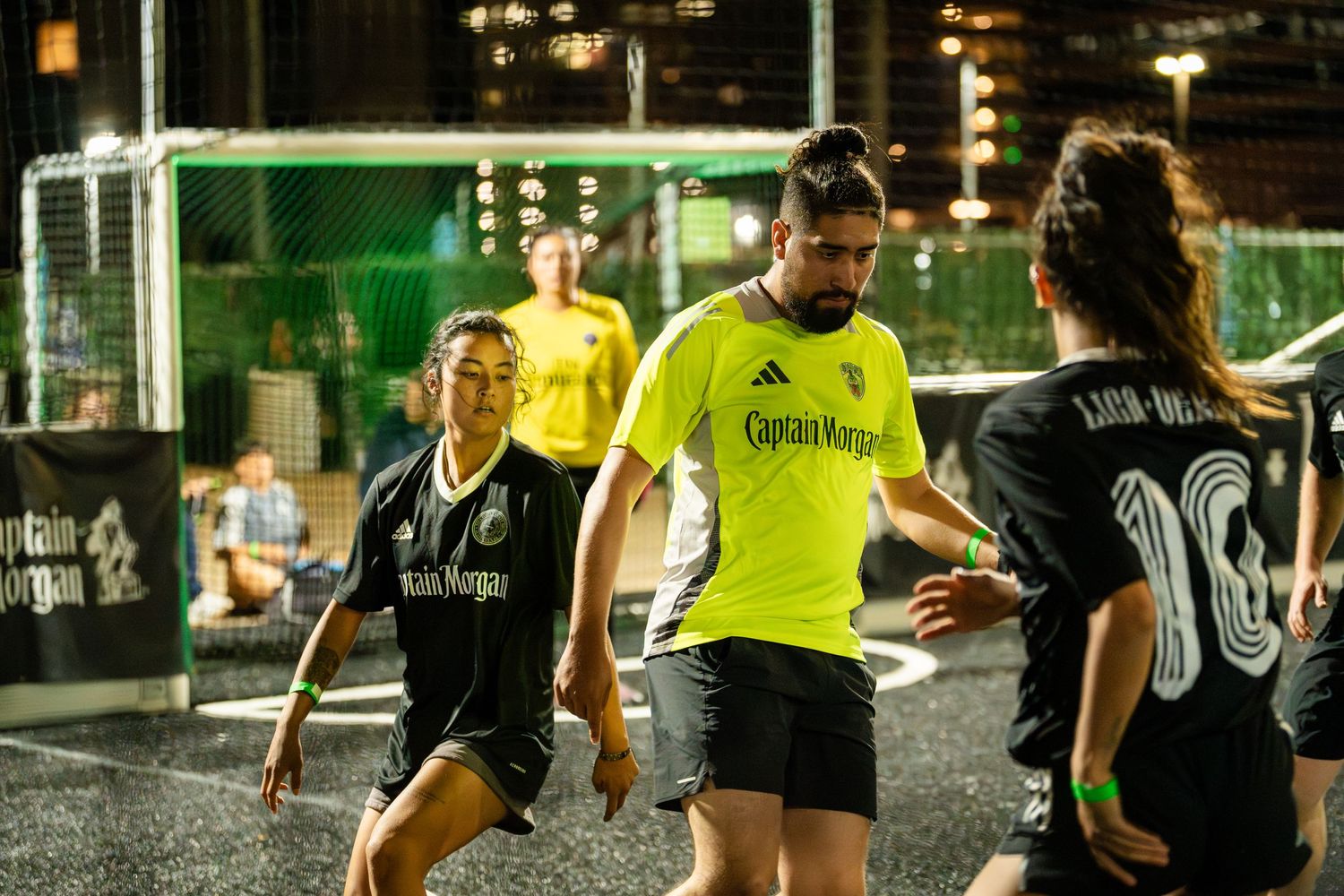 Indoor soccer players compete with one player in bright yellow jersey controlling the ball.
