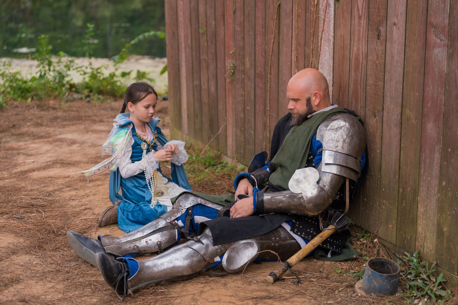 Medieval scene with costumed performers resting by wooden fence at renaissance faire.