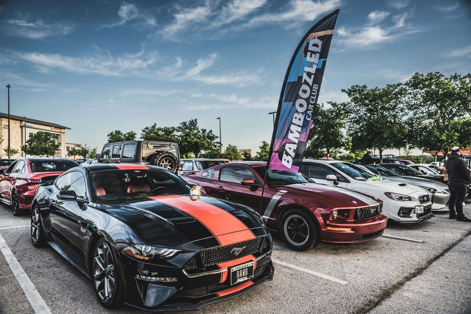 Custom modified sports cars lined up at a car show with black and orange racing stripes.