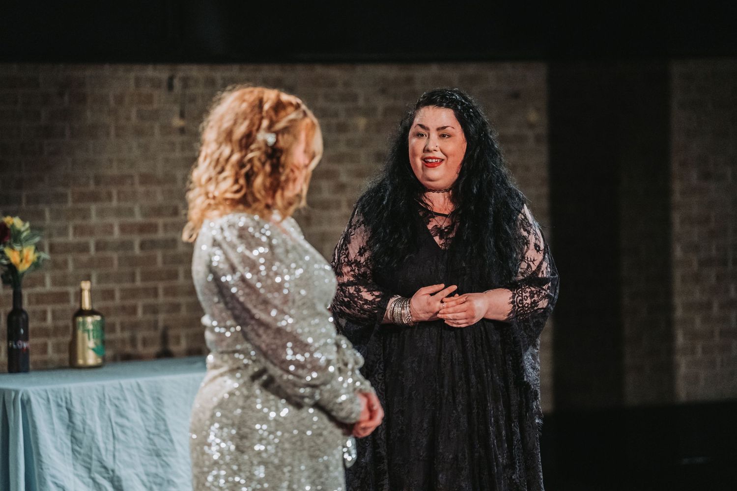 Two actors in lace and sparkly dresses perform an emotional scene on stage.