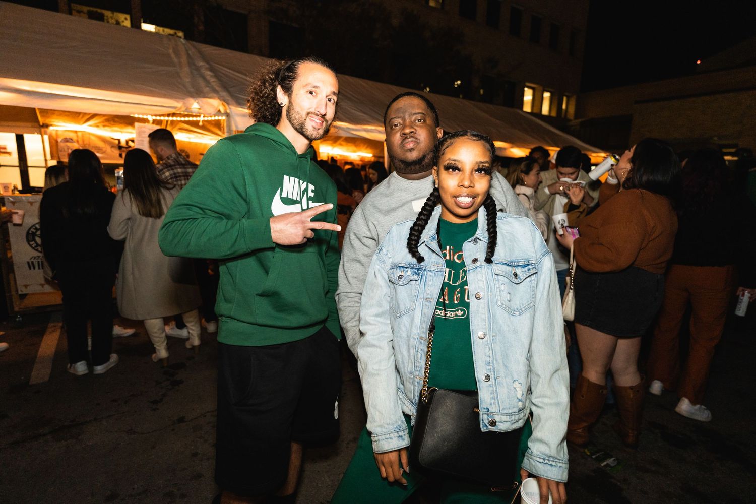 Three friends in casual wear posing together at an outdoor evening event.