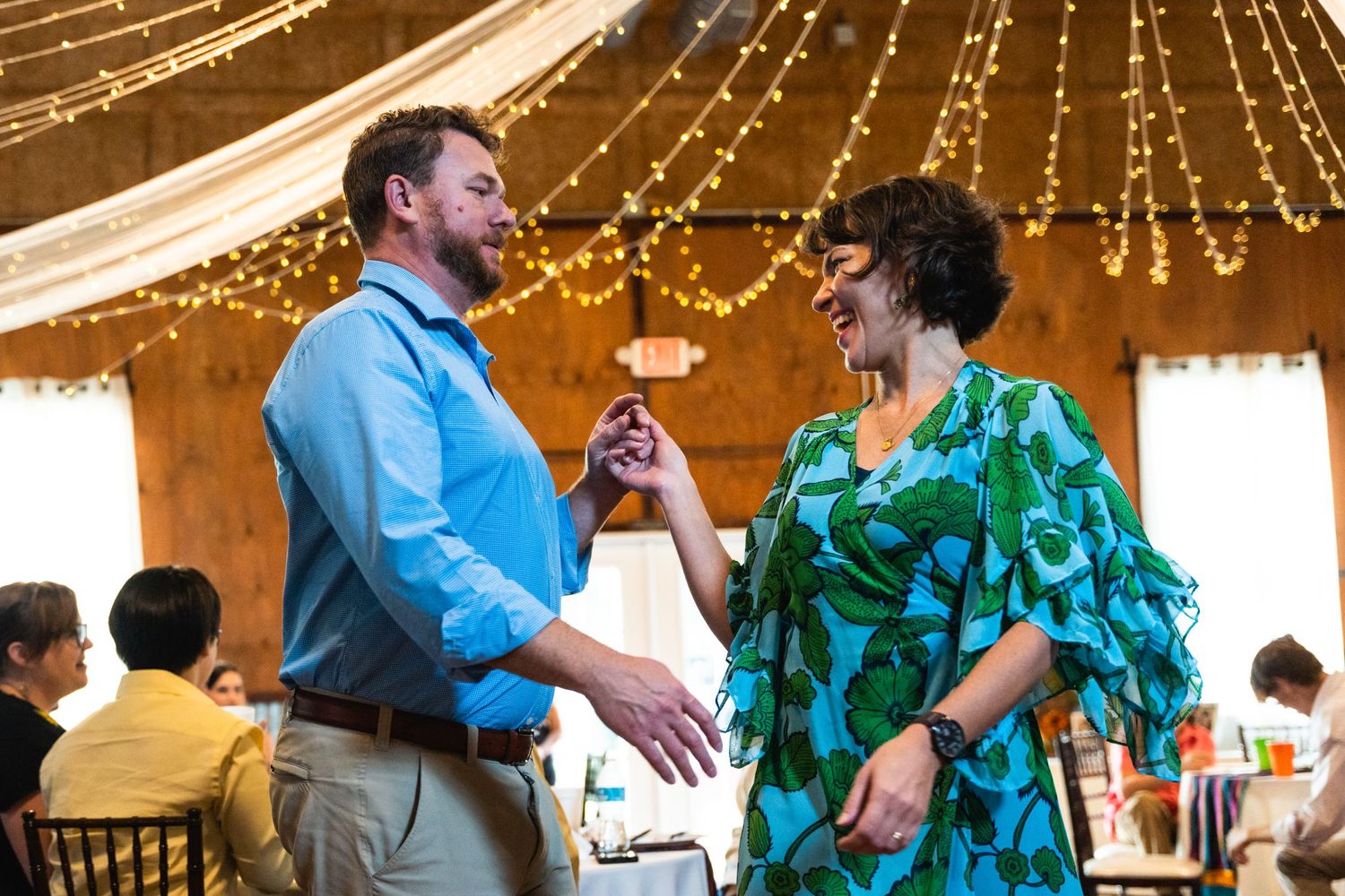 Guests dancing together under string lights at a rustic wedding reception venue.