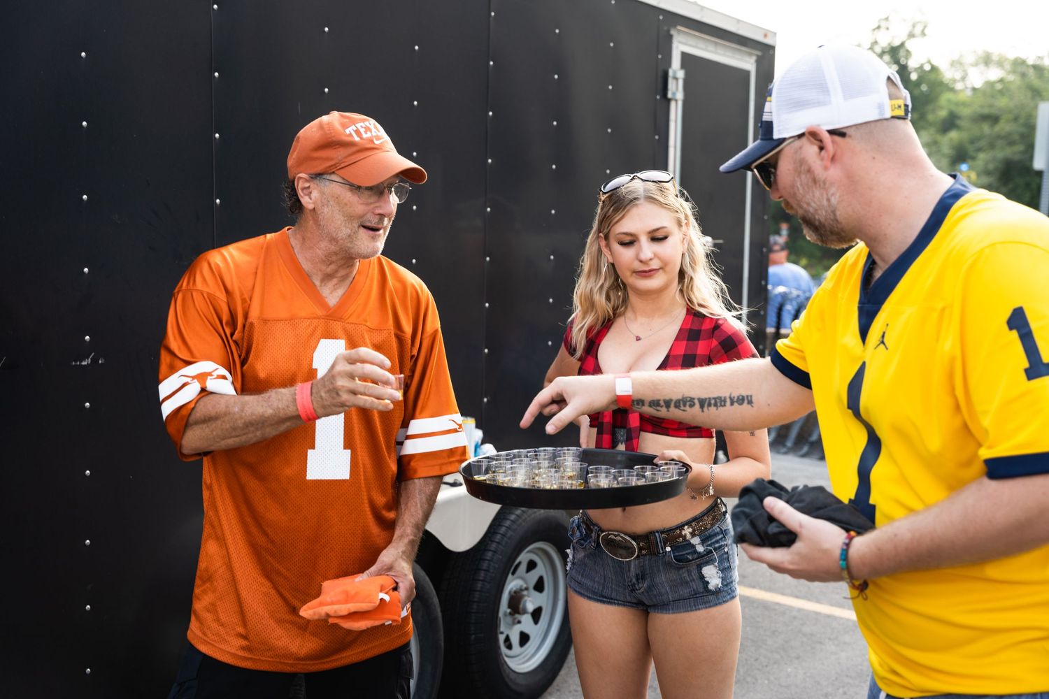 Group serves drinks from a black trailer at an outdoor tailgating event.