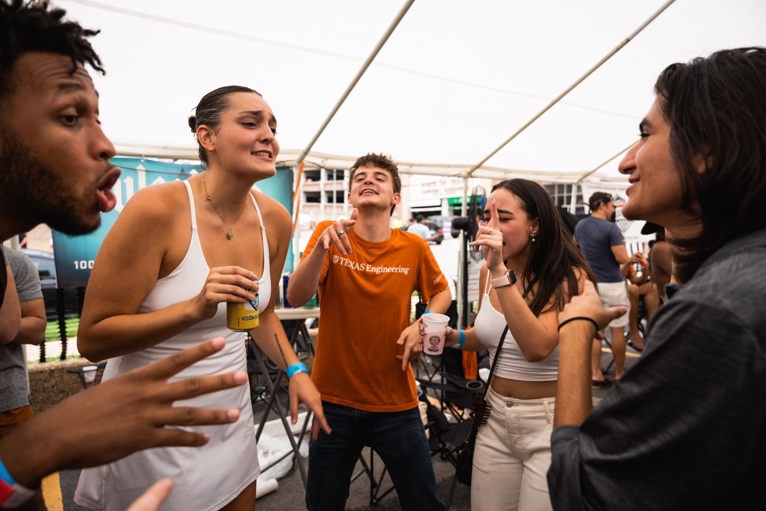 Friends enjoying drinks and socializing together at an outdoor party under a white tent.