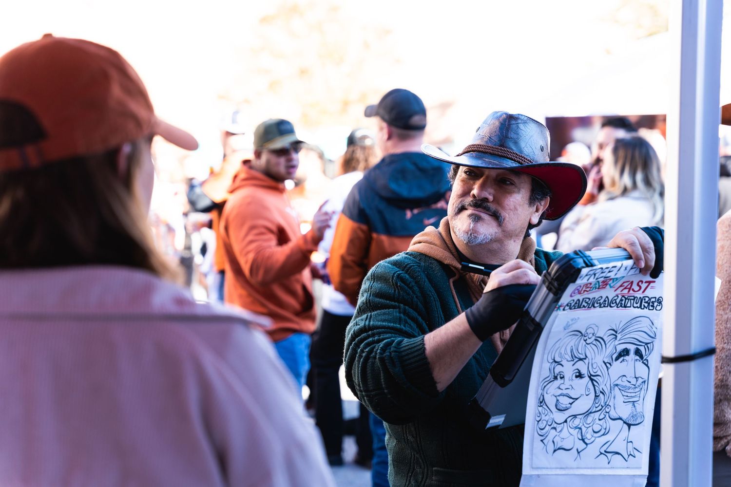 People interacting at an outdoor vendor booth during a tailgate party.