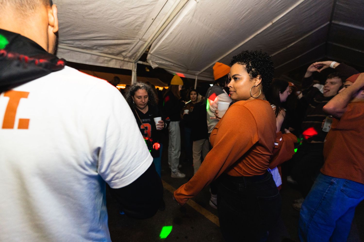 Crowd dancing under dimly lit tent with orange and white attire visible.
