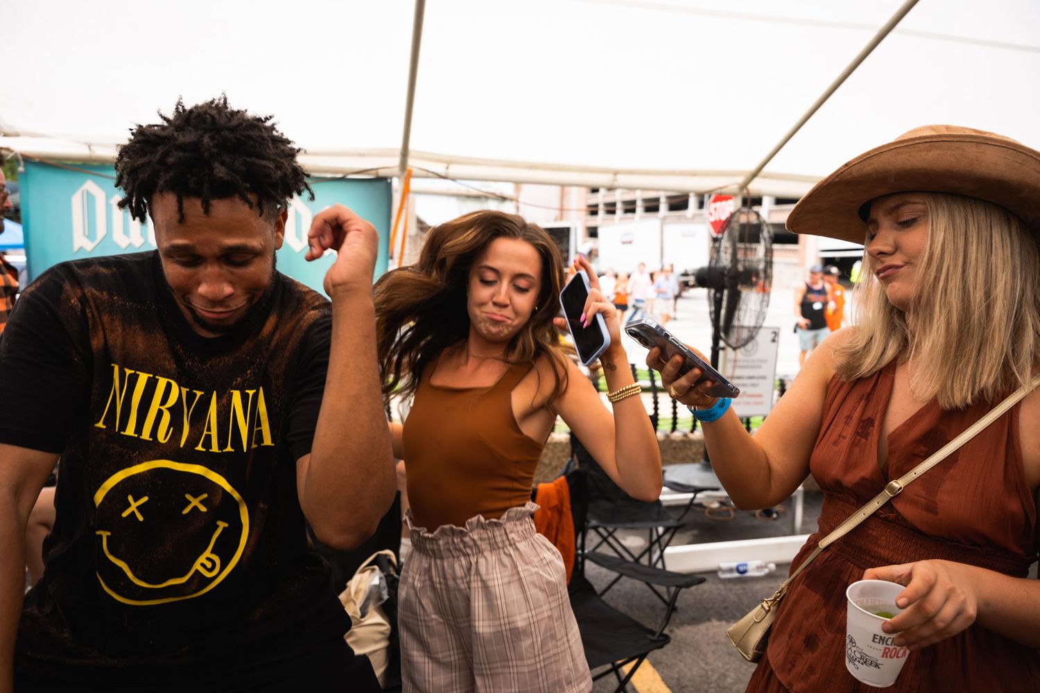 Party-goers dancing and having fun at an outdoor music festival under a tent.