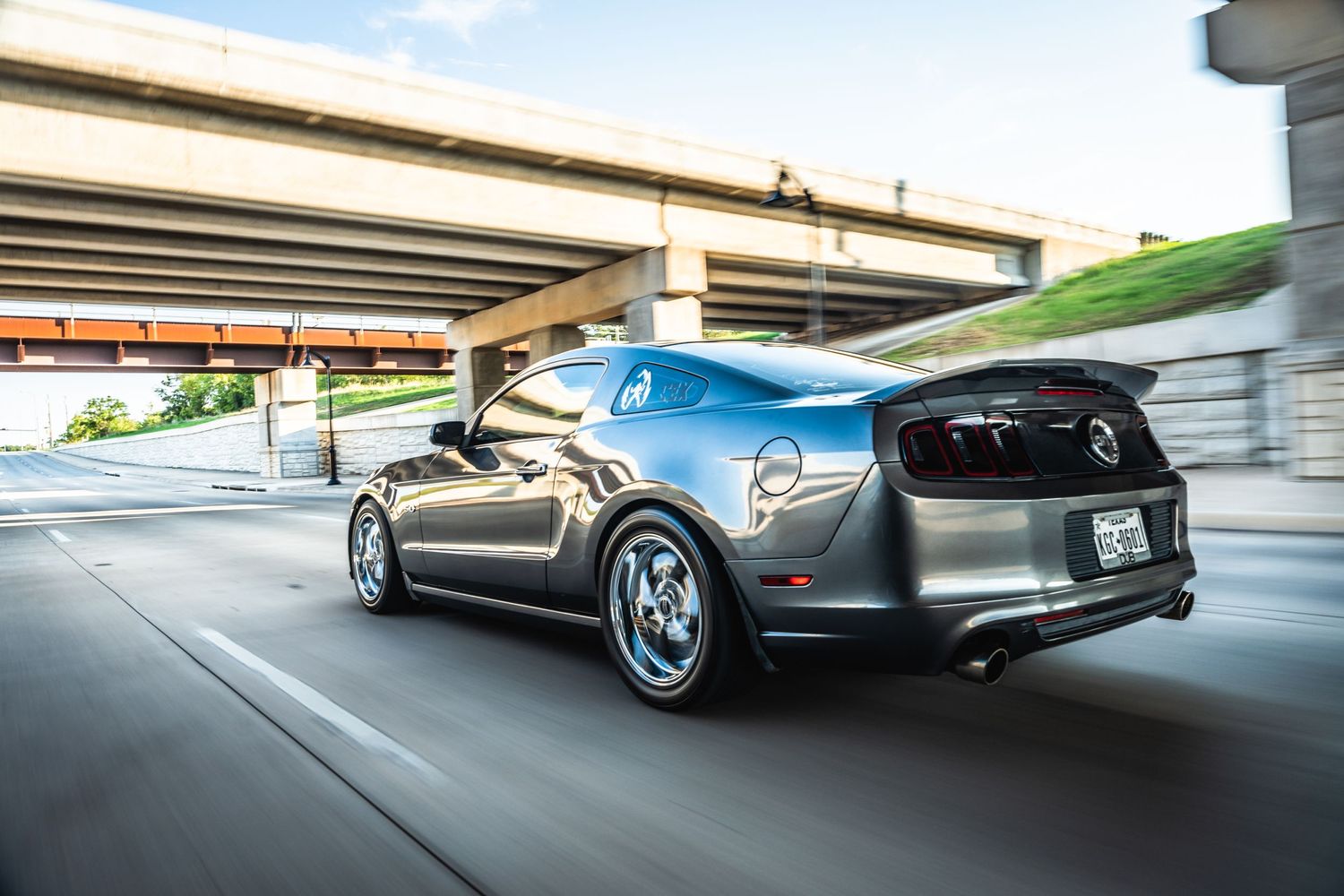 Gray Dodge Charger with aftermarket wheels and exhaust driving under bridge.