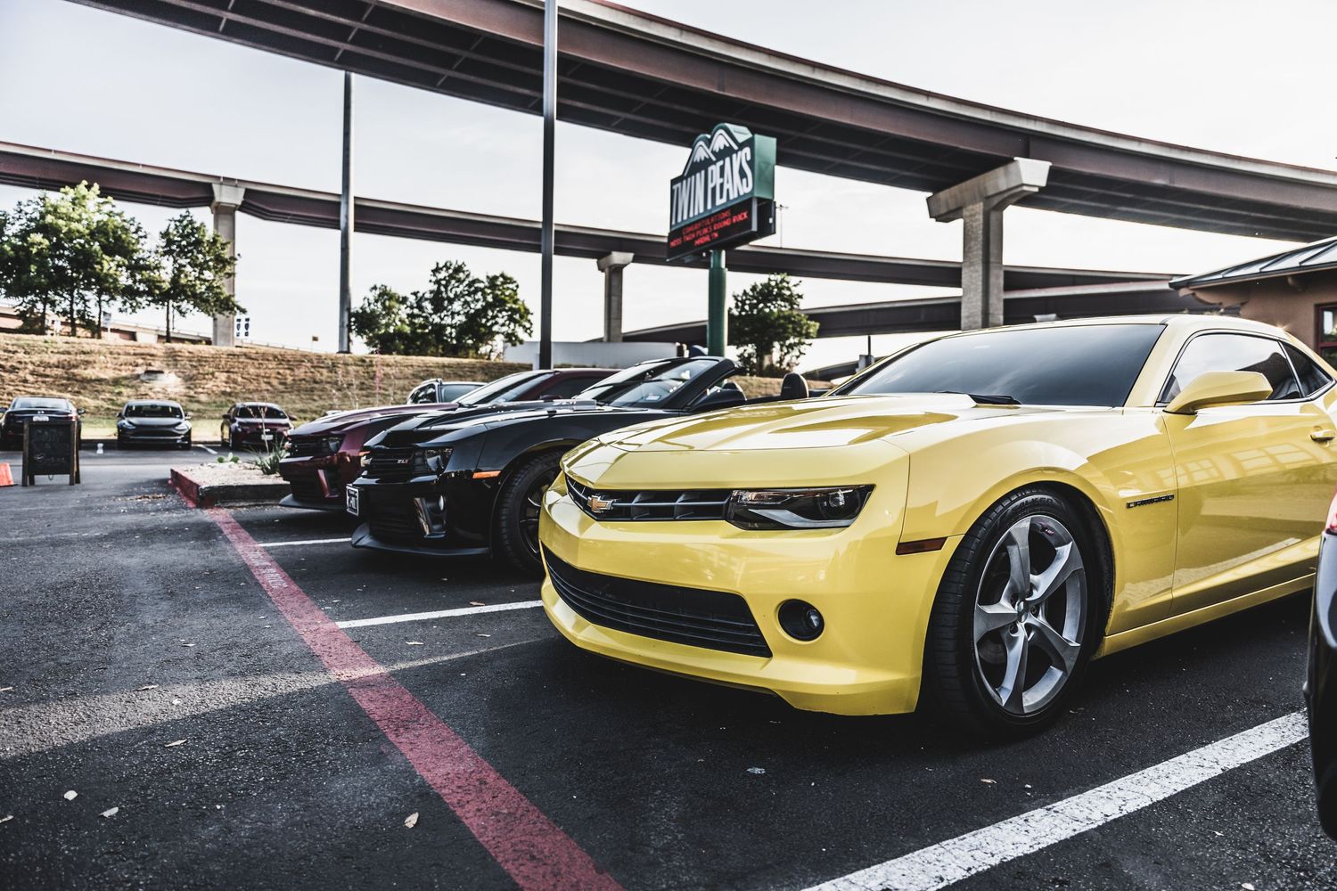 Yellow and black Chevrolet Camaros parked side by side under an overpass.