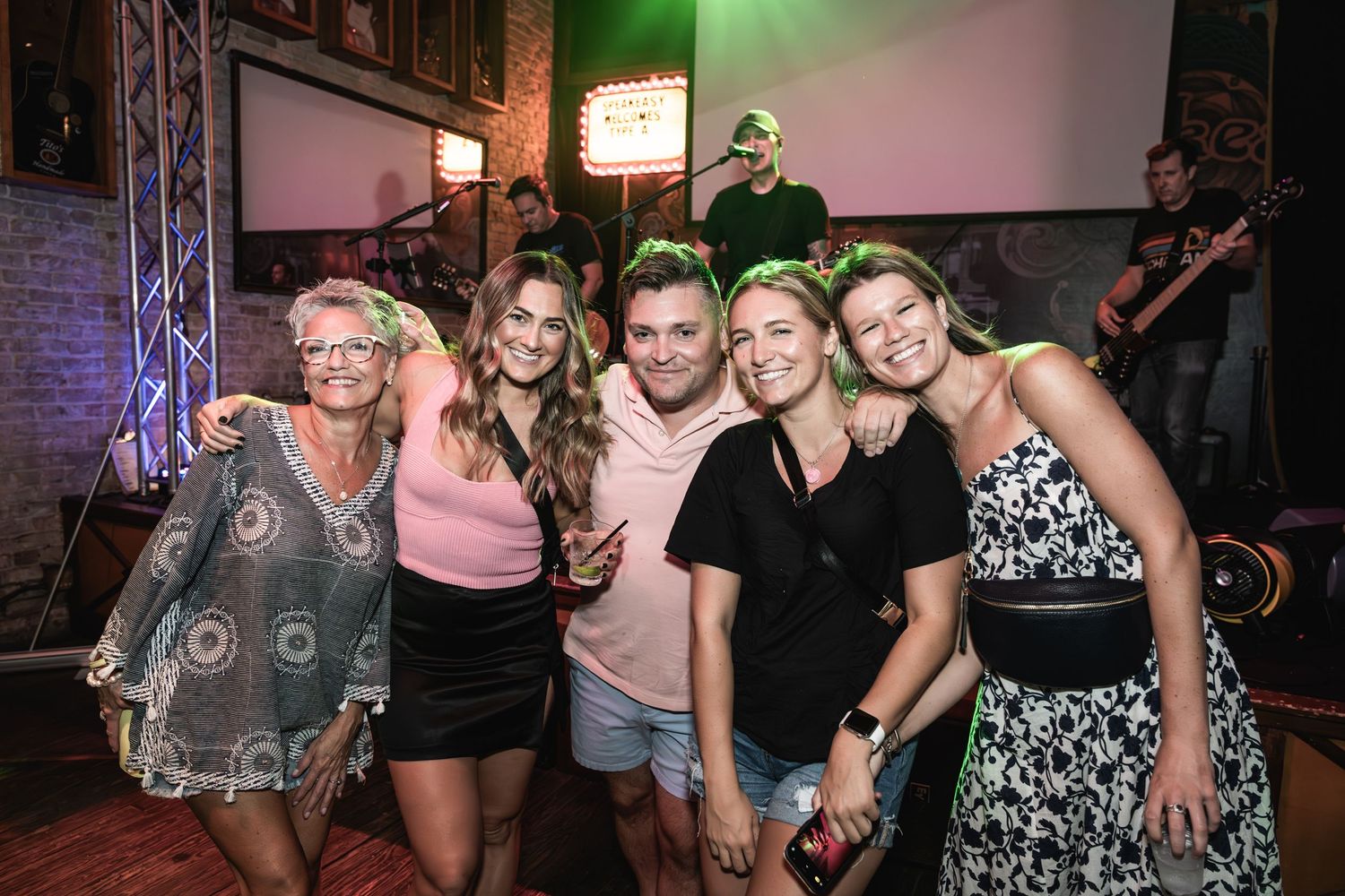 Group of friends posing together at a nightclub with stage lighting and entertainment equipment visible.