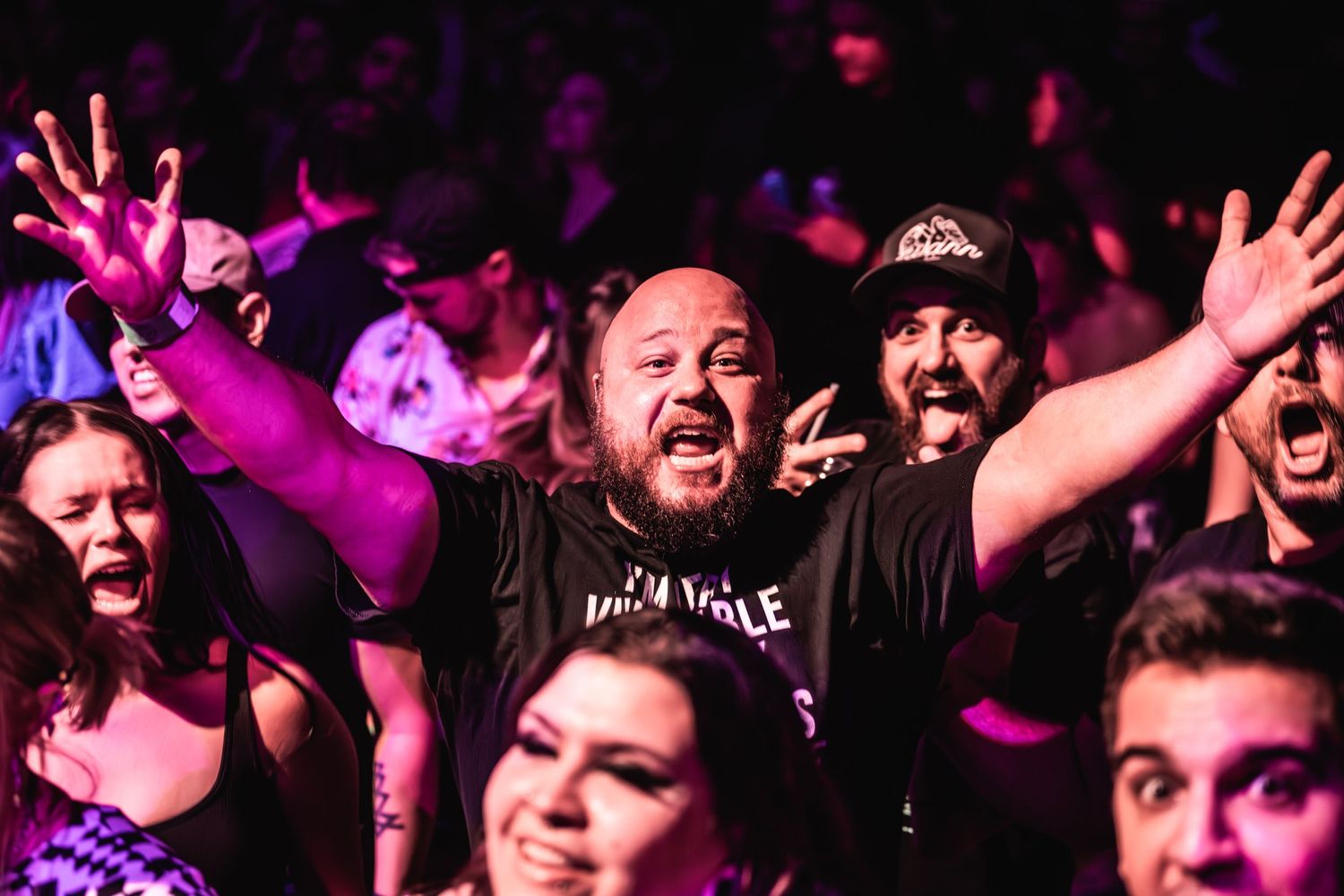 Concert audience members cheer enthusiastically during performance under red lighting.