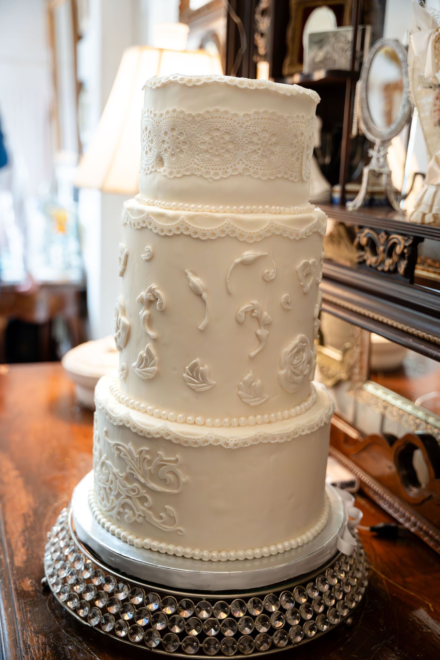 Elegant three-tier white wedding cake with delicate lace details on silver stand.