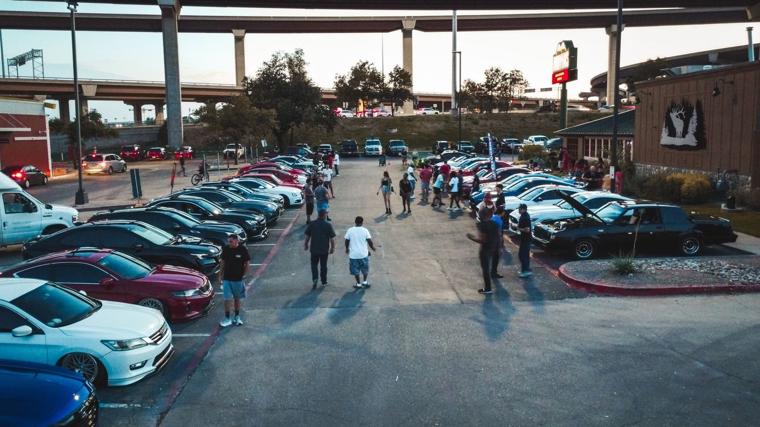 Overhead shot of a car meetup showing attendees gathered between rows of parked vehicles.