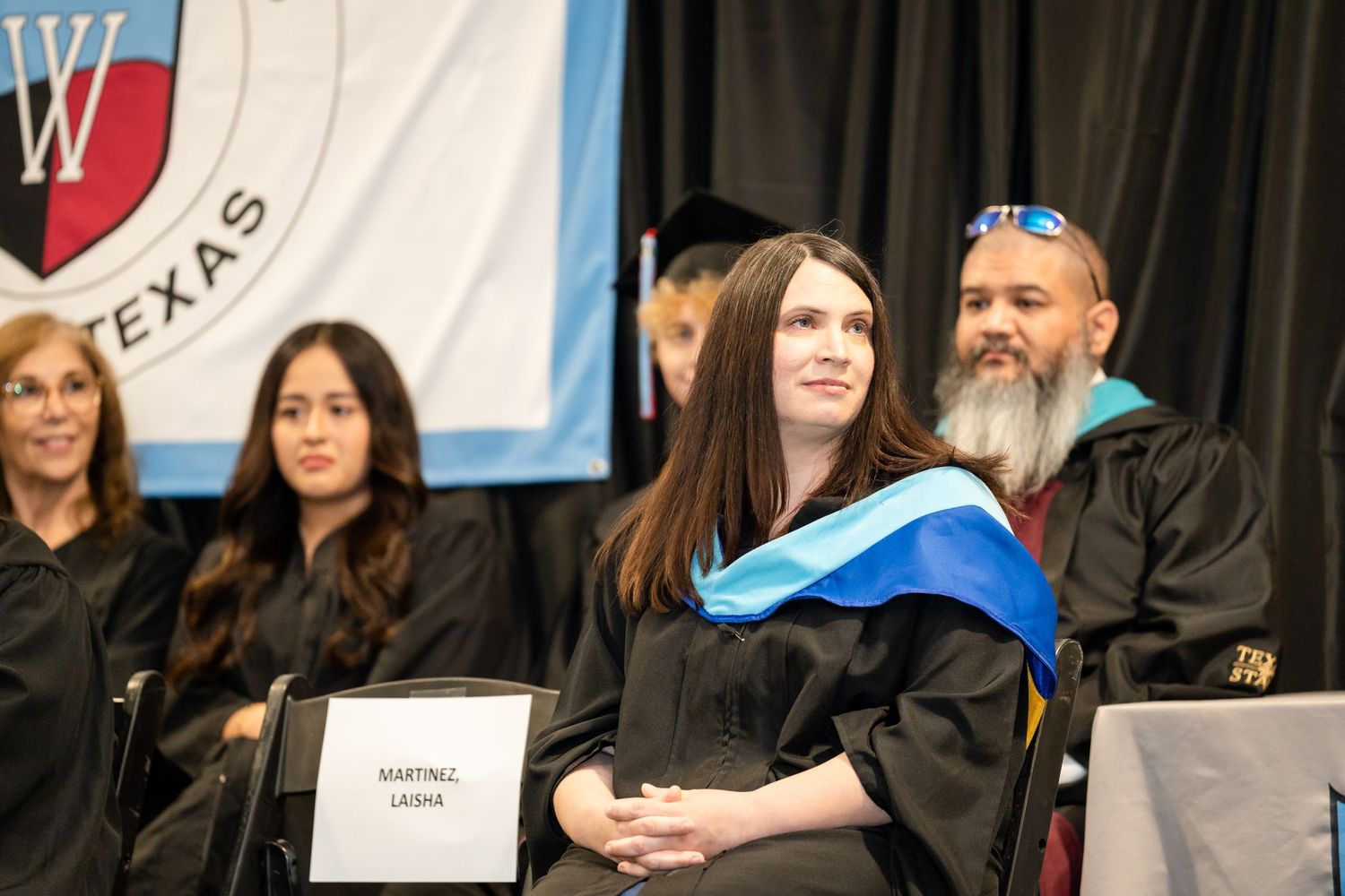 Faculty and graduates seated during graduation ceremony with university banner in background.