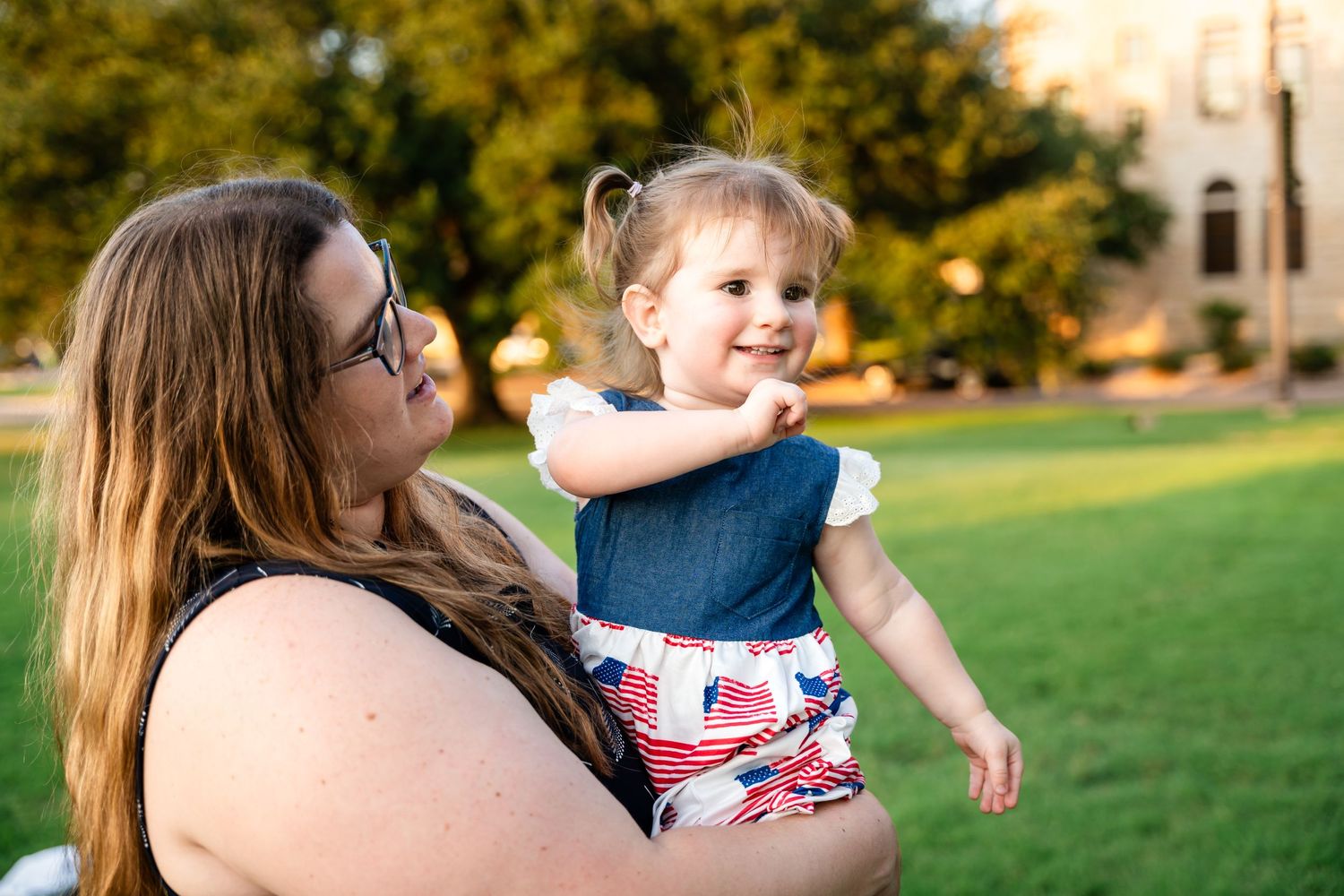 A tender outdoor moment shared on a sunny day with green grass and trees in the background.