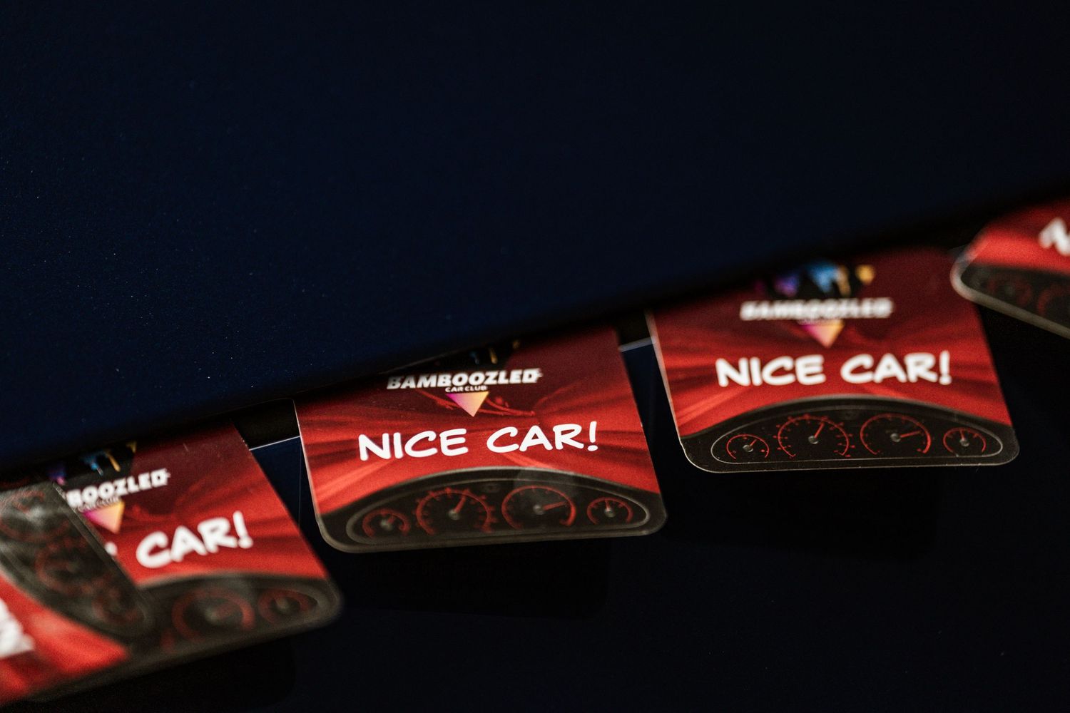 Close-up of red 'NICE CAR!' stickers arranged in a row against dark background.
