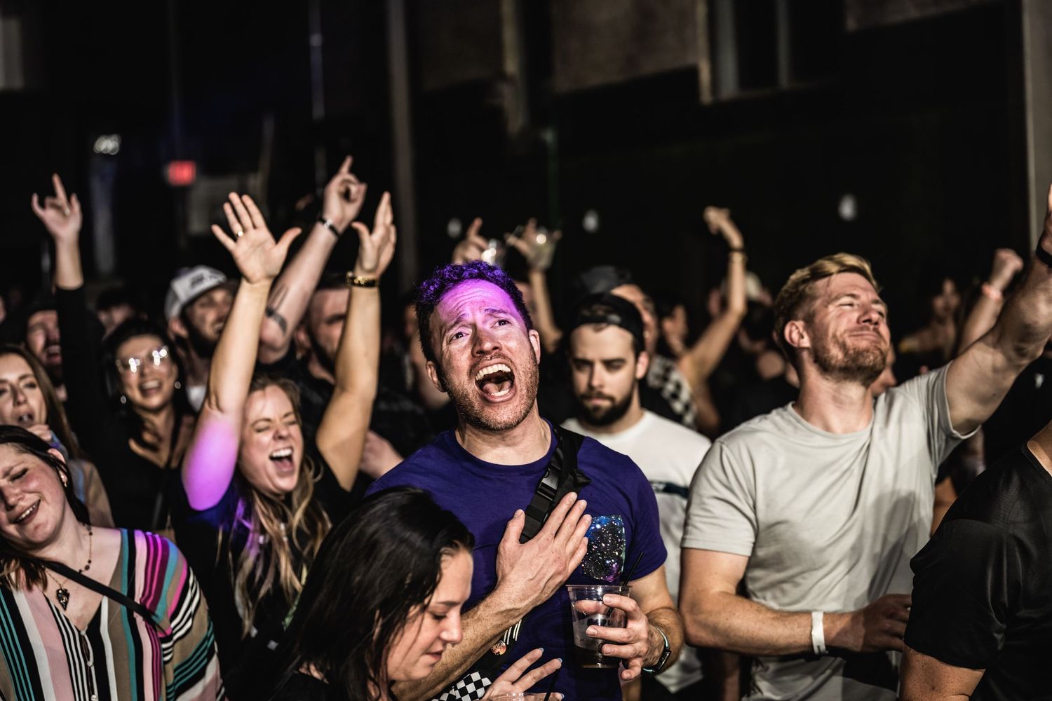 Passionate concert audience cheering and raising hands during energetic live performance.