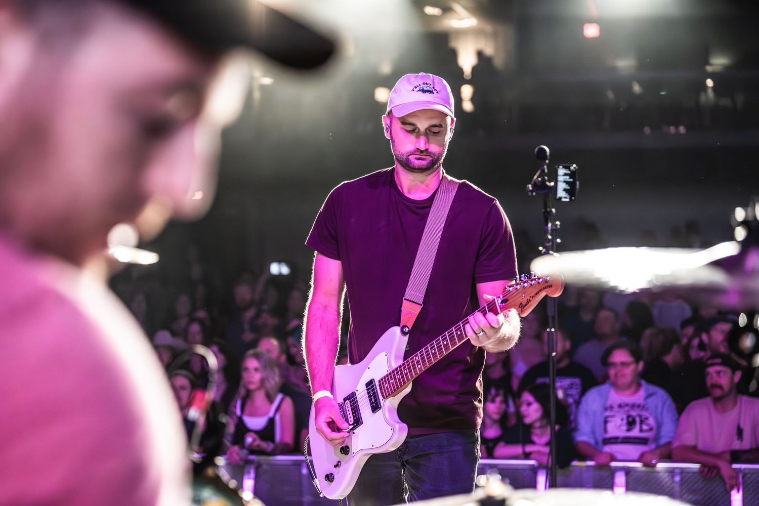 A guitarist performs on stage bathed in purple lighting while a crowd watches from below.