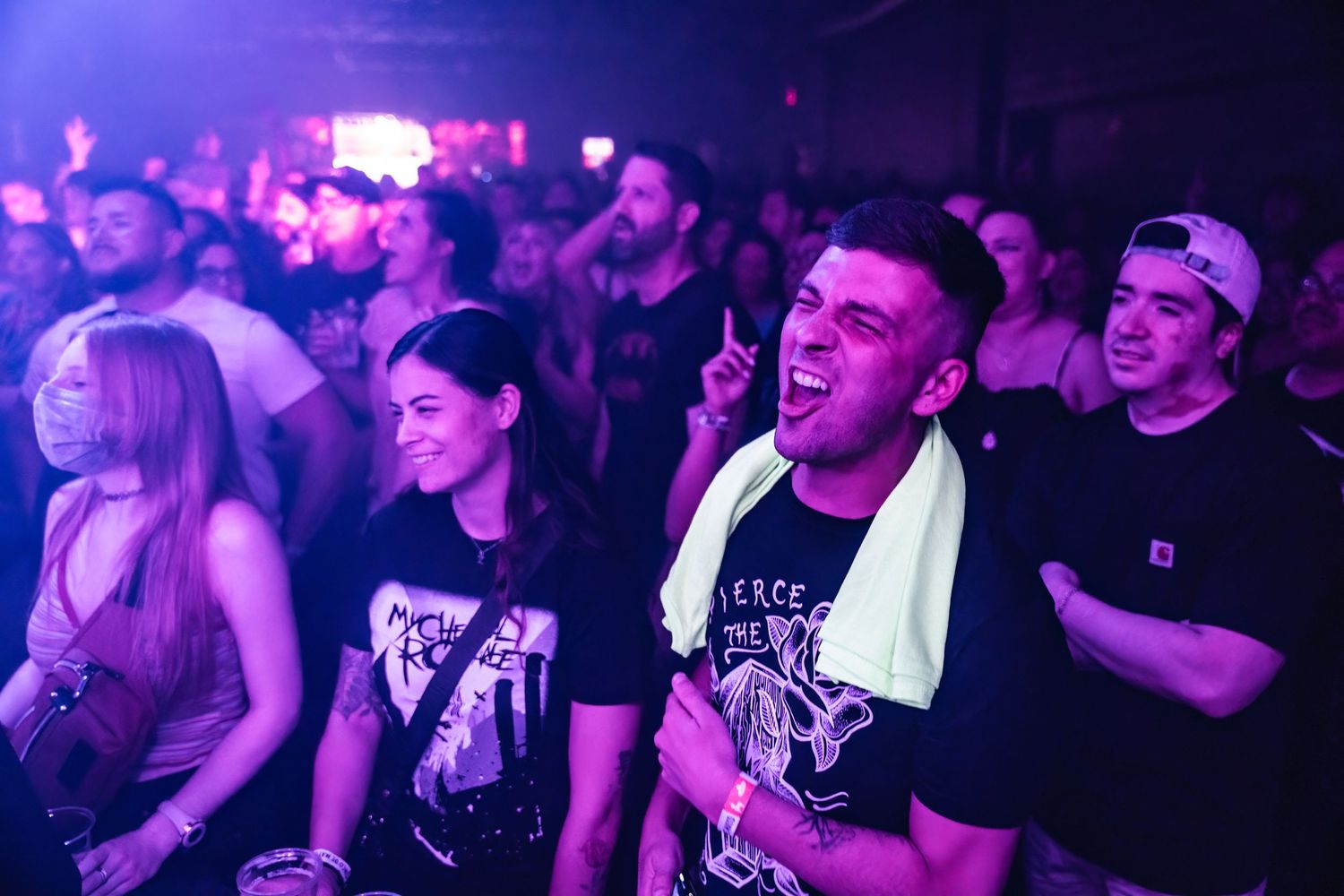 Enthusiastic concert crowd reacts with excitement under purple venue lighting.