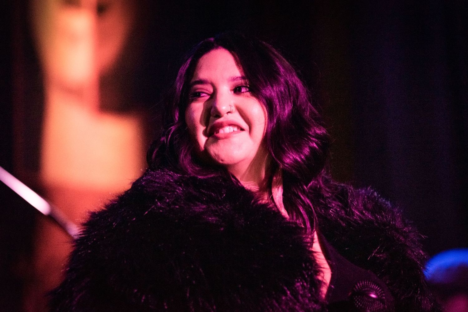 A performer illuminated by red stage lights smiles during a live show.