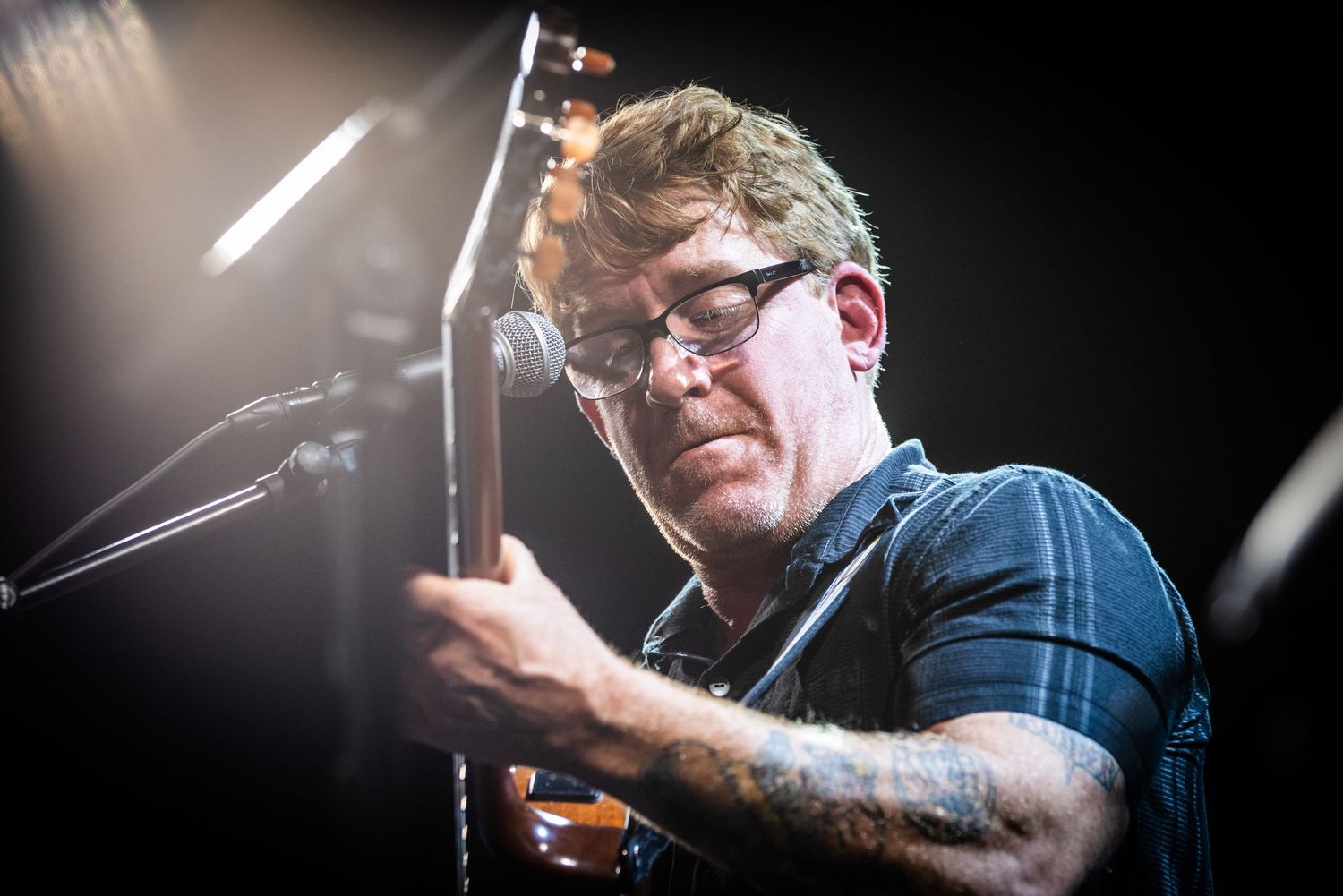 Performer plays guitar under dramatic stage lighting during concert.