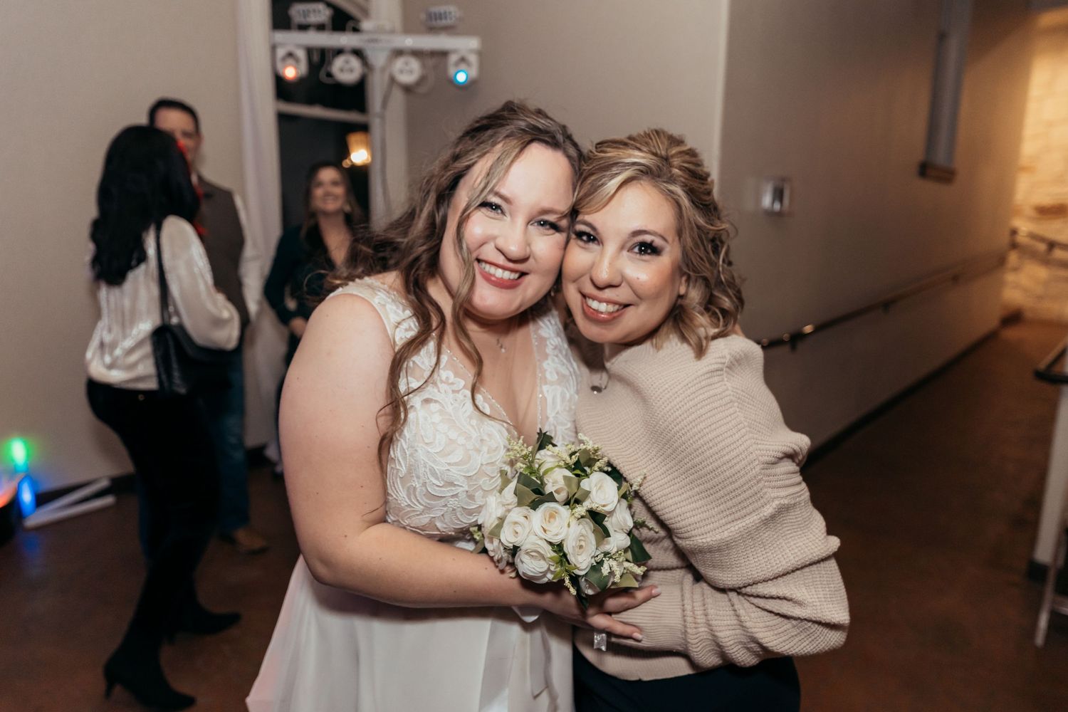 Two guests sharing a joyful embrace while holding a wedding bouquet.