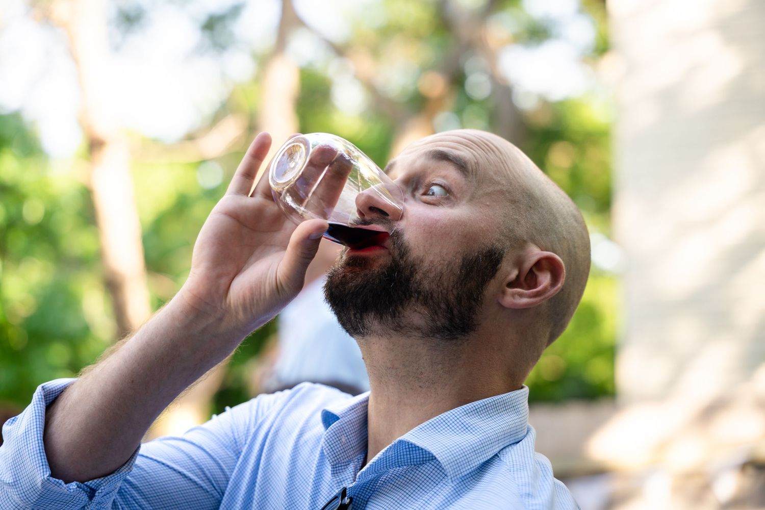Guest with beard enjoying wine during outdoor celebration.