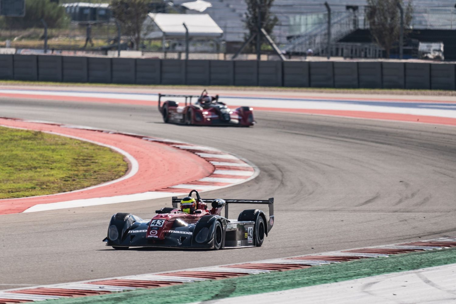 Two formula-style race cars navigate through a red-bordered racing circuit turn.