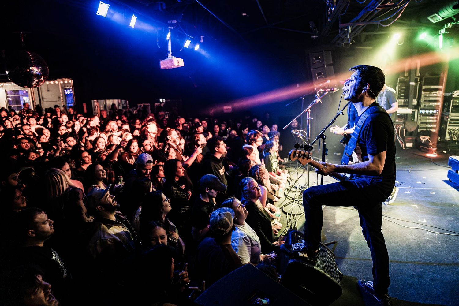 Rock musician performs on stage to packed crowd under blue stage lights at energetic concert venue.