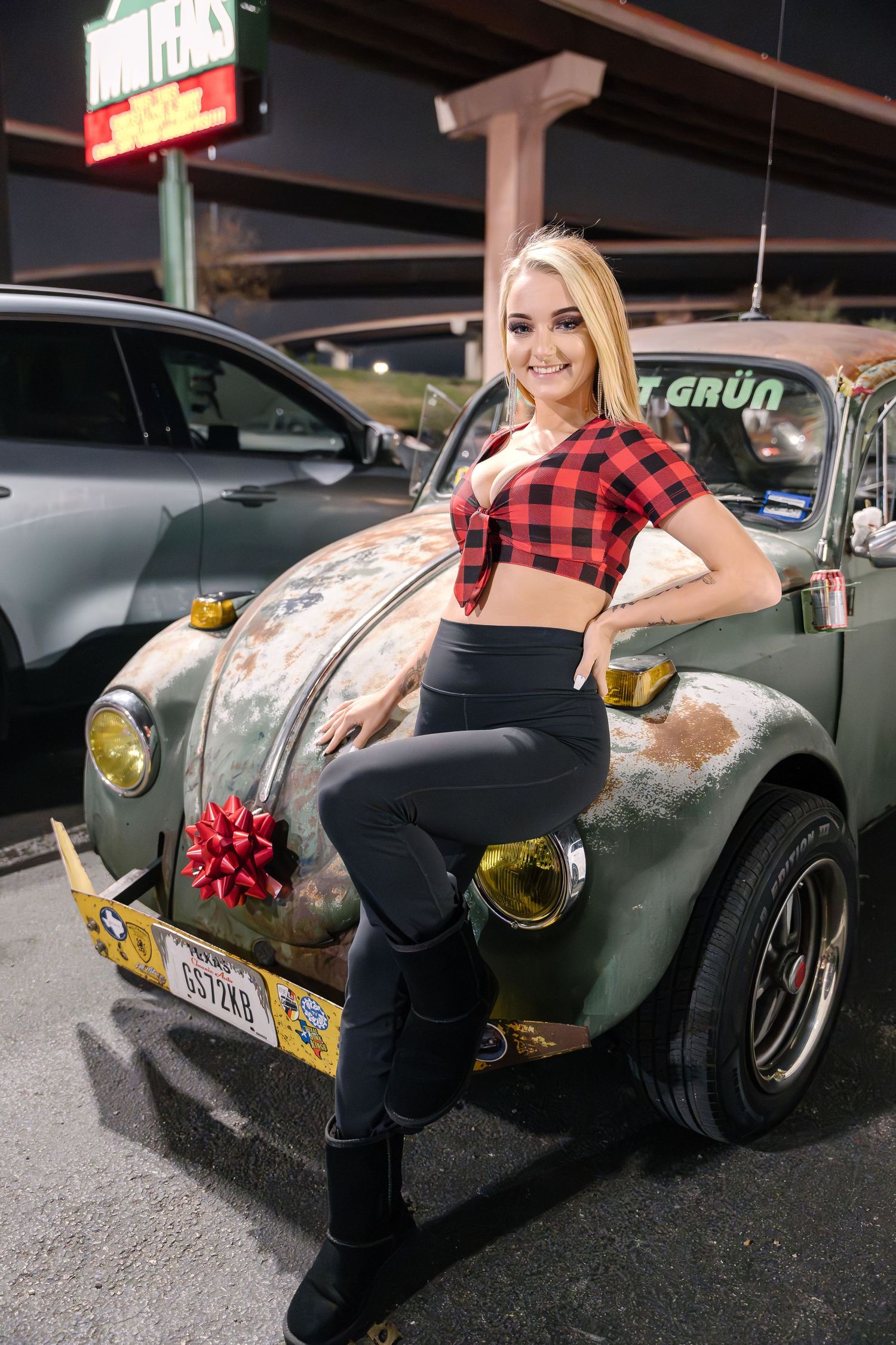 Person in plaid crop top posing with vintage beetle car in parking lot.