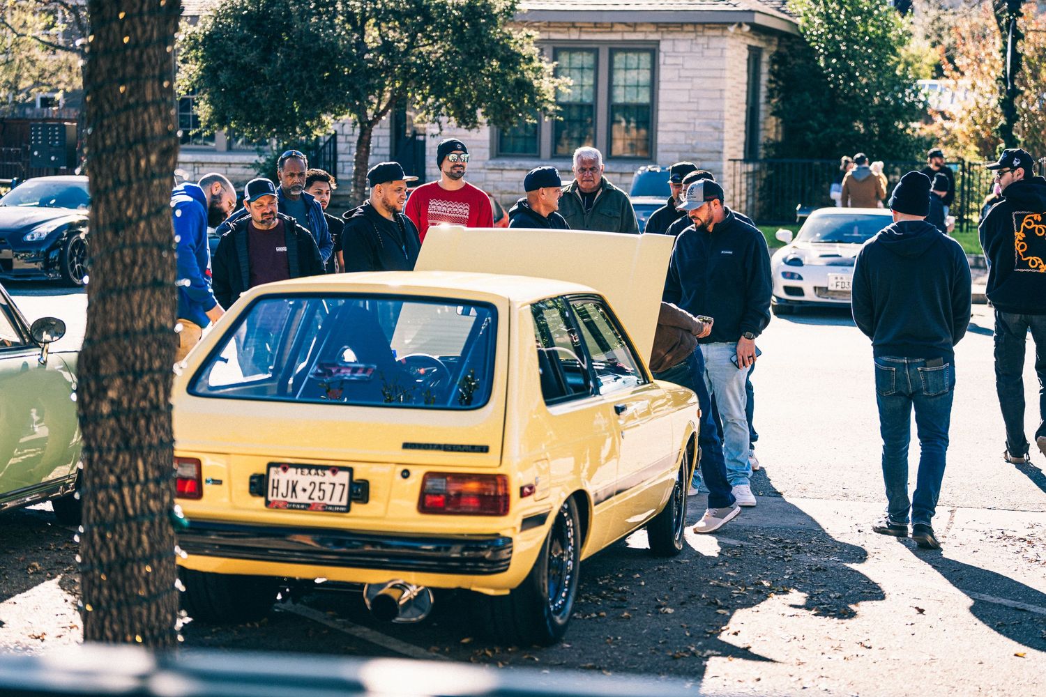Yellow vintage Toyota Starlet hatchback surrounded by onlookers at a car meet.