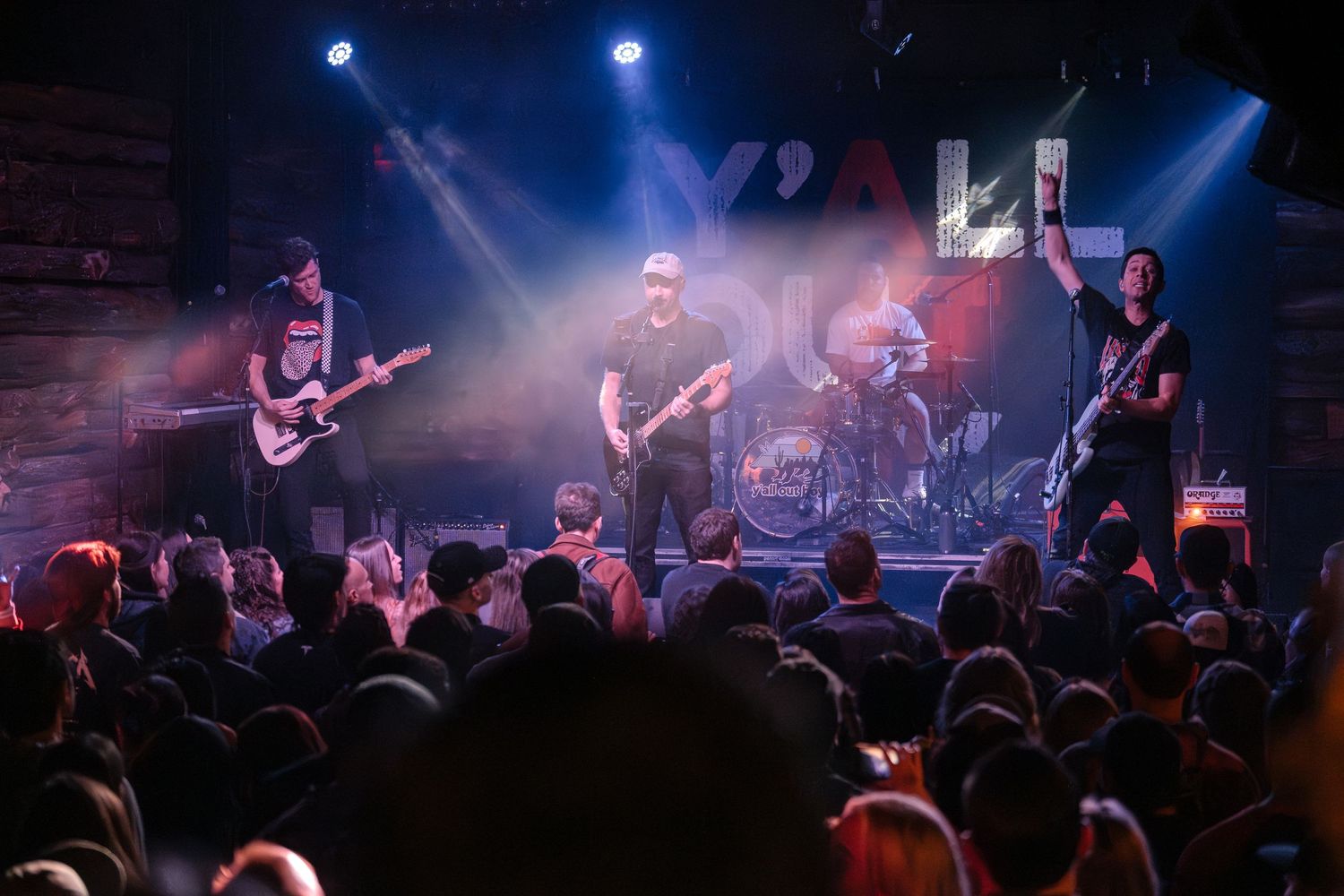 A rock band performs on stage with dramatic blue lighting as the crowd watches from below.