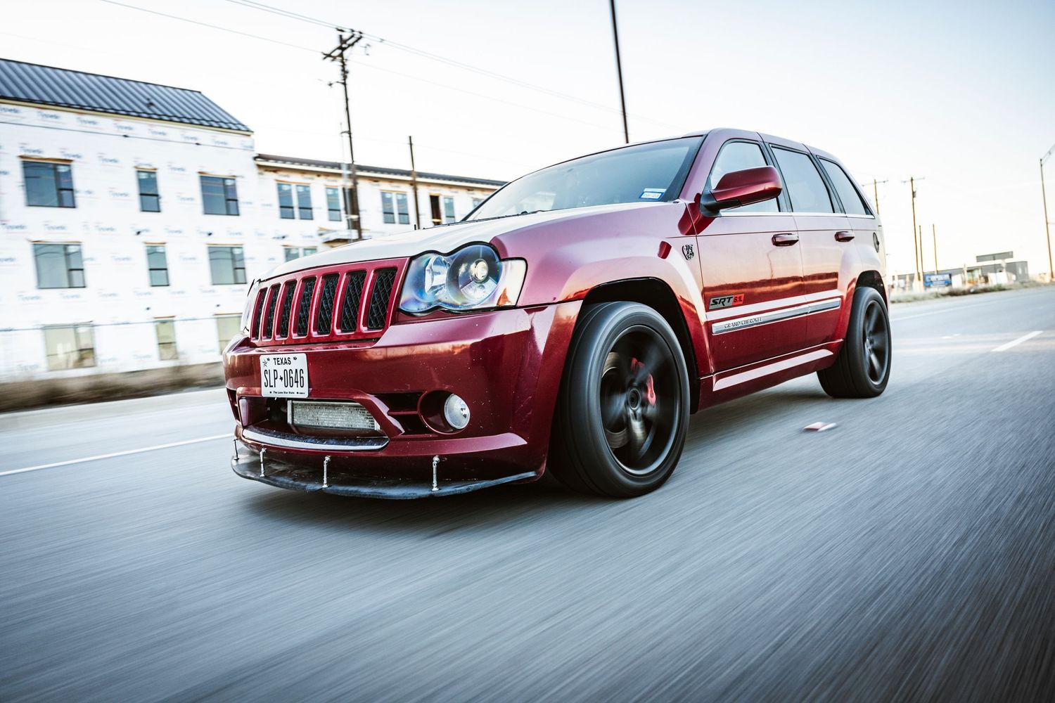 Red Jeep Grand Cherokee SRT with custom black wheels driving on city street.
