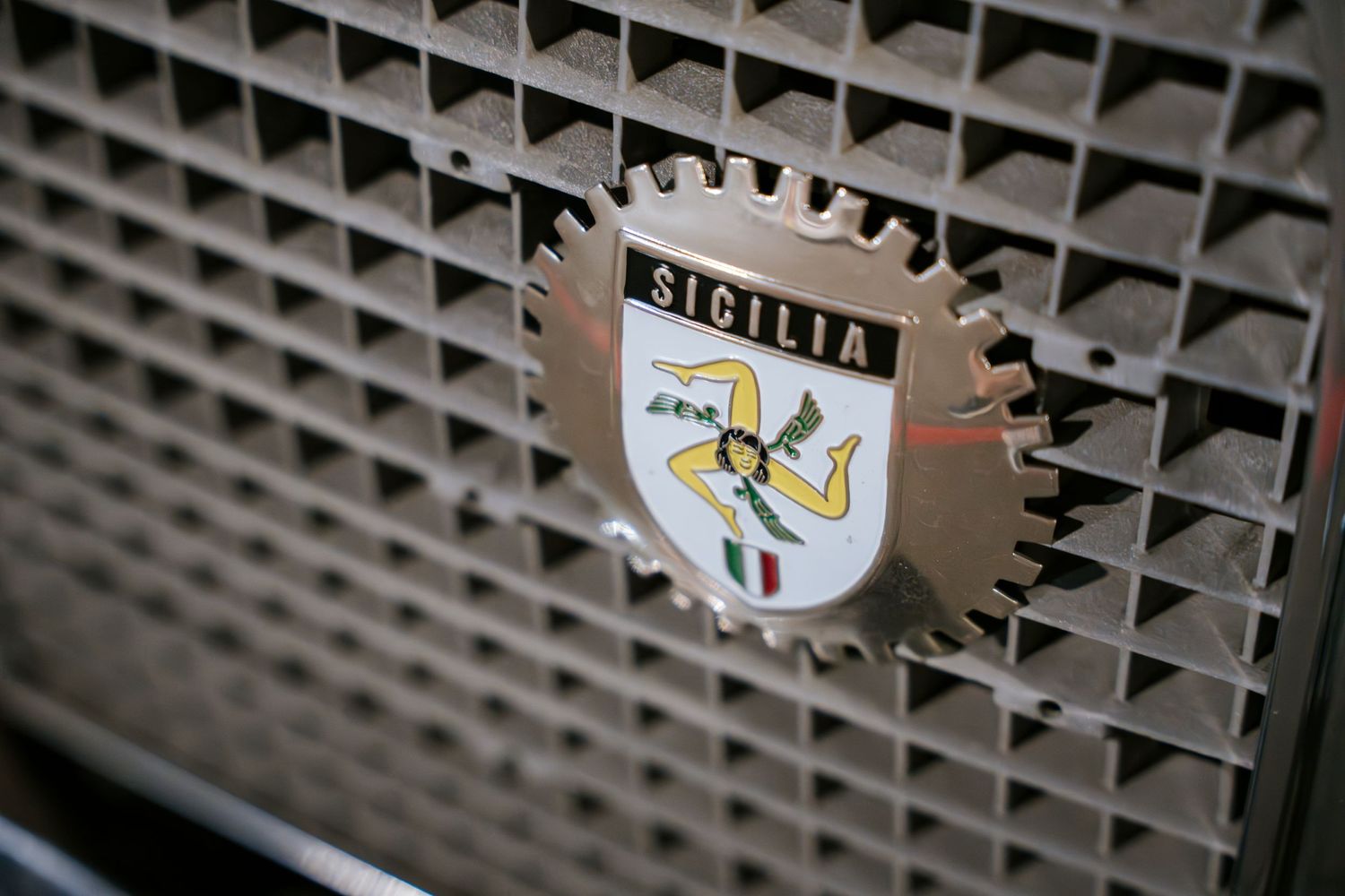 Sicilia badge detail on vintage car grille with metallic finish.