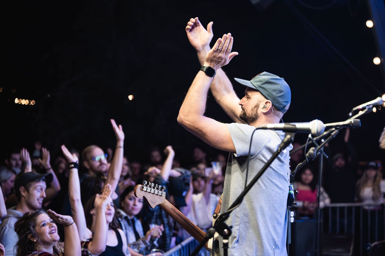 Performer clapping hands above head while crowd cheers at music concert.