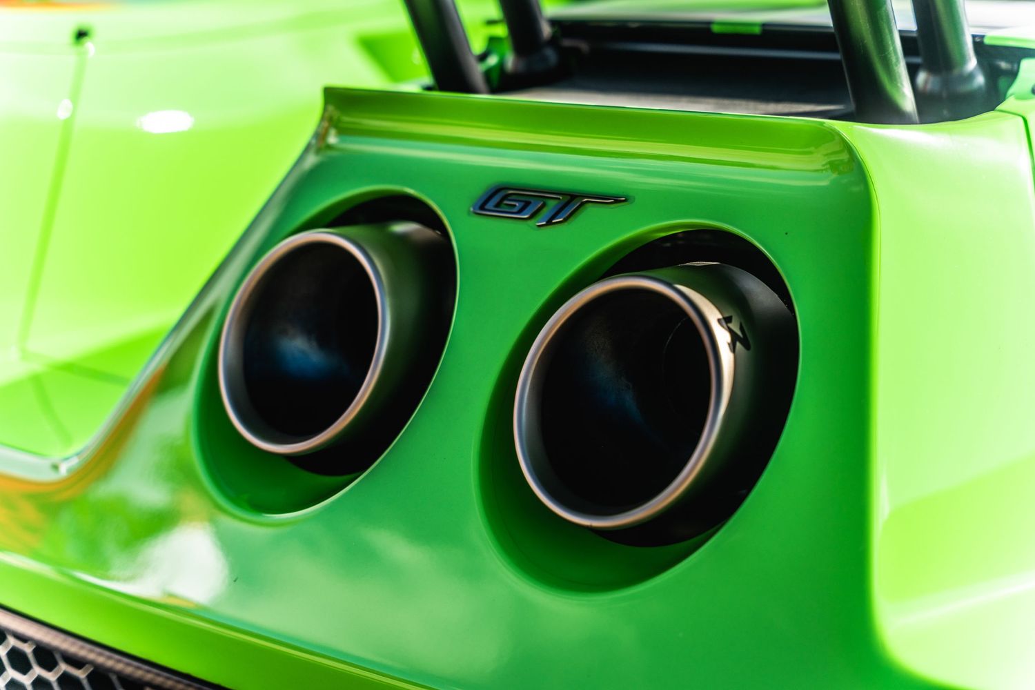 Dramatic close-up of dual black exhaust tips on a lime green sports car.