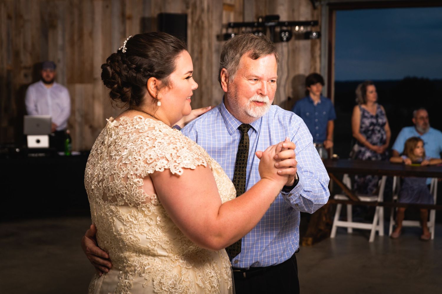 A couple dances together at their wedding reception while guests watch from tables in the background.