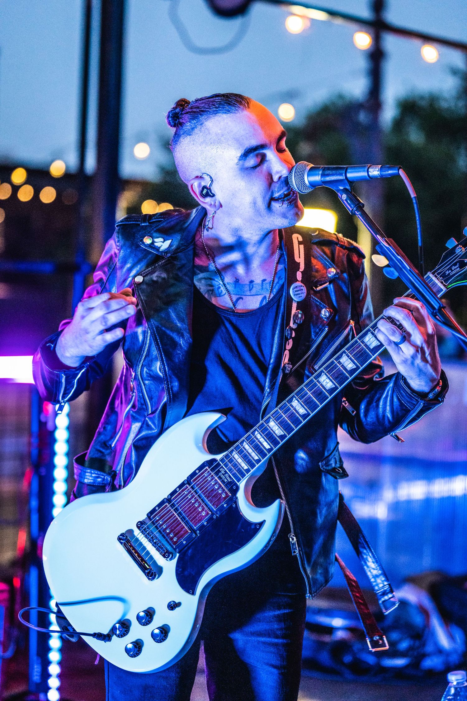 Musician playing white guitar while singing on stage with blue lighting.